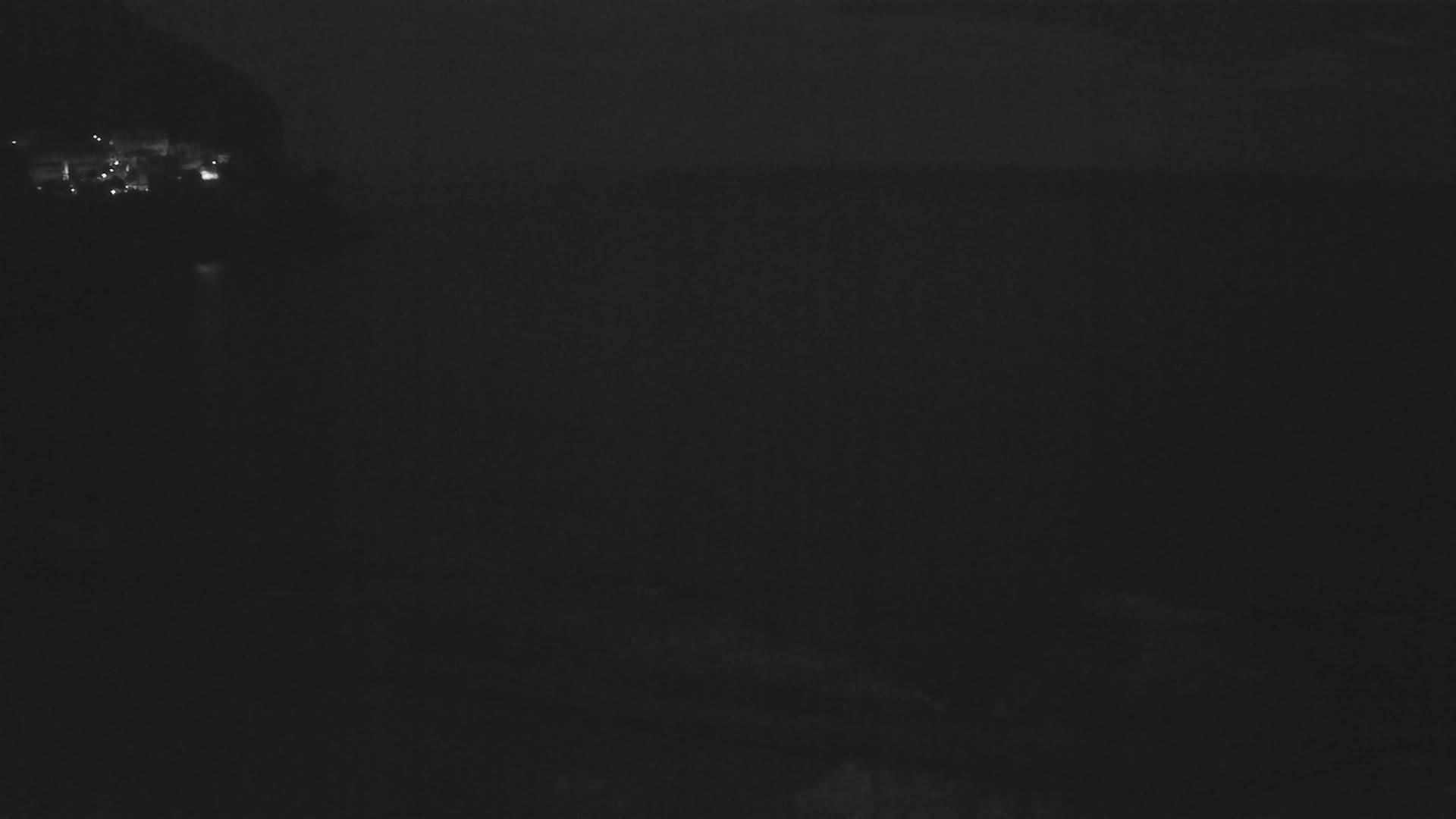 A dark, nighttime scene shows a body of water with faintly visible lights on the far shore.