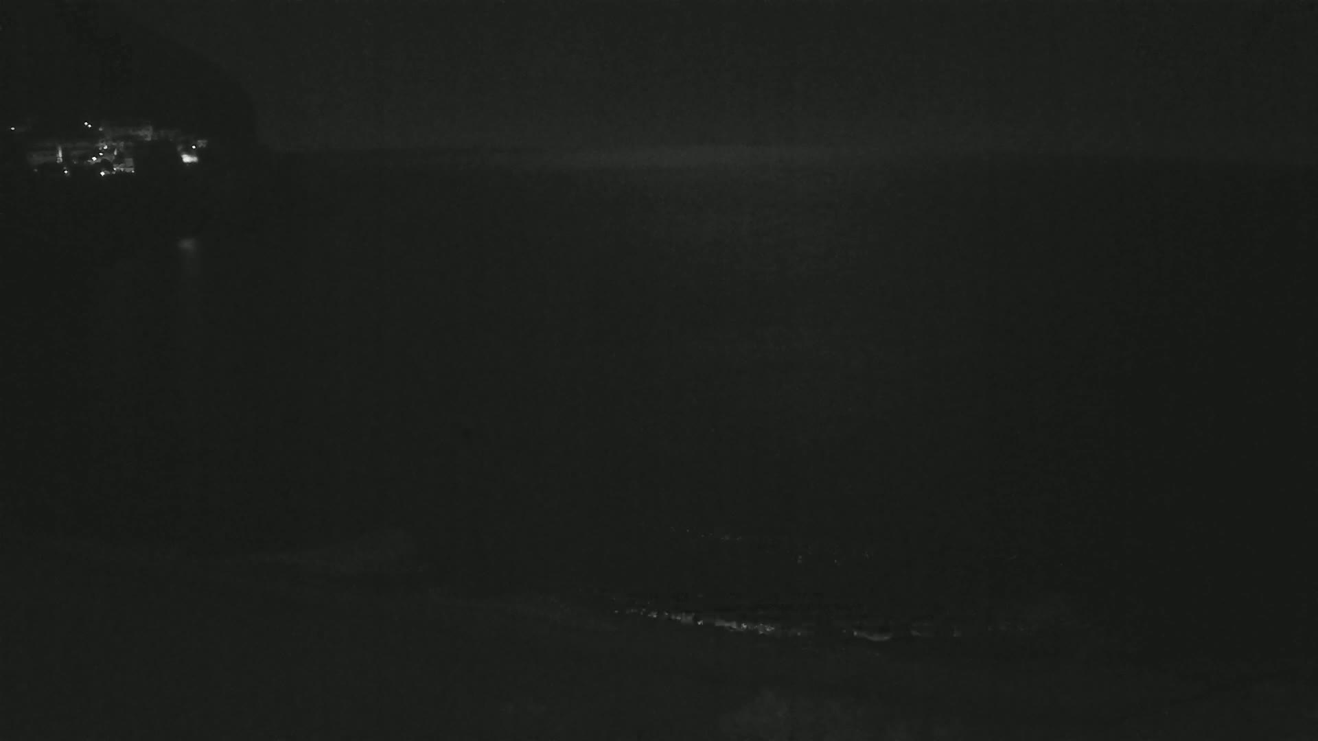 A dark, nighttime view of a coastline with faintly visible lights in the distance.