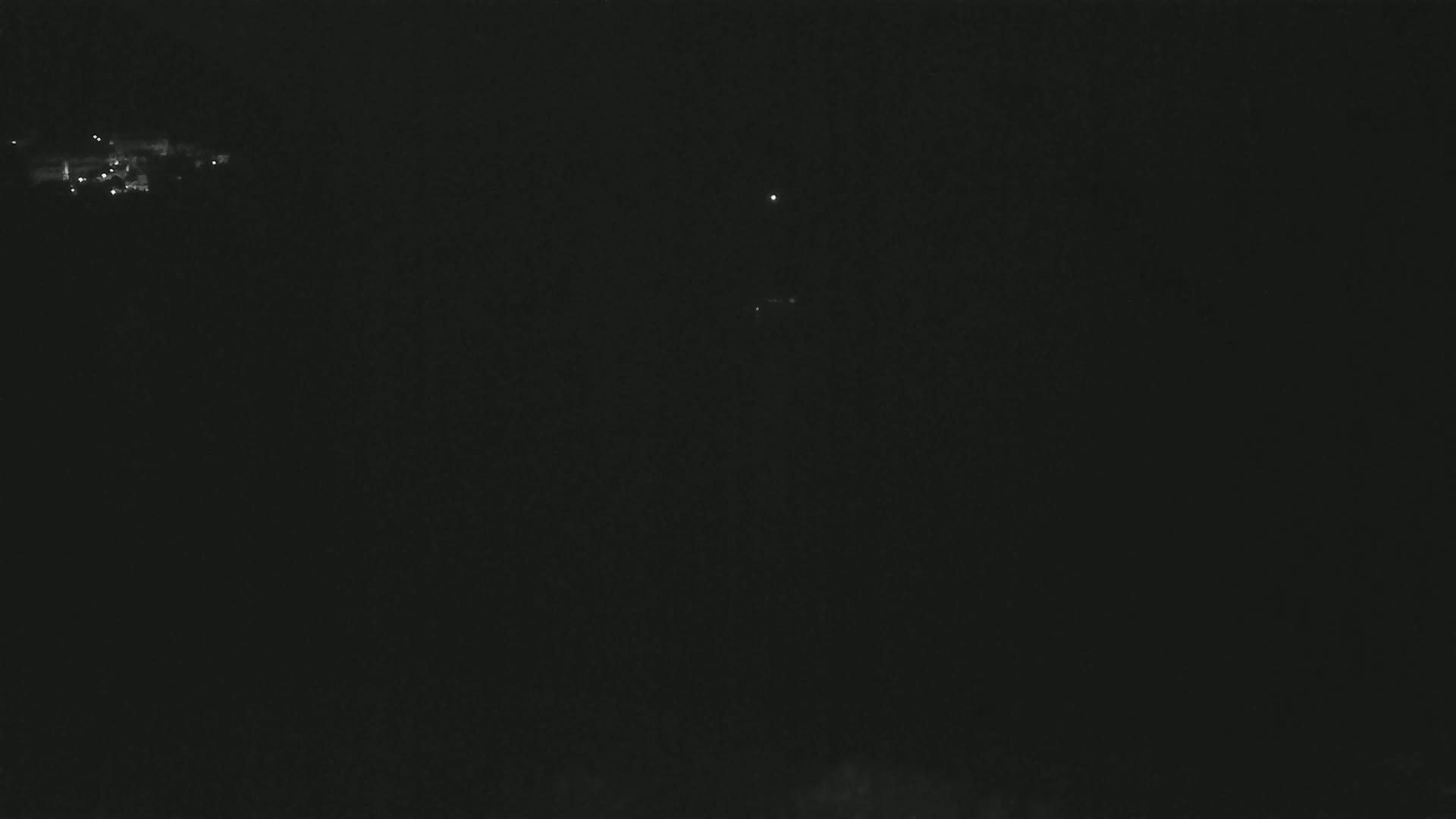 A dark nighttime scene shows a few distant lights, possibly a town or city, with a bright star or planet visible in the sky.