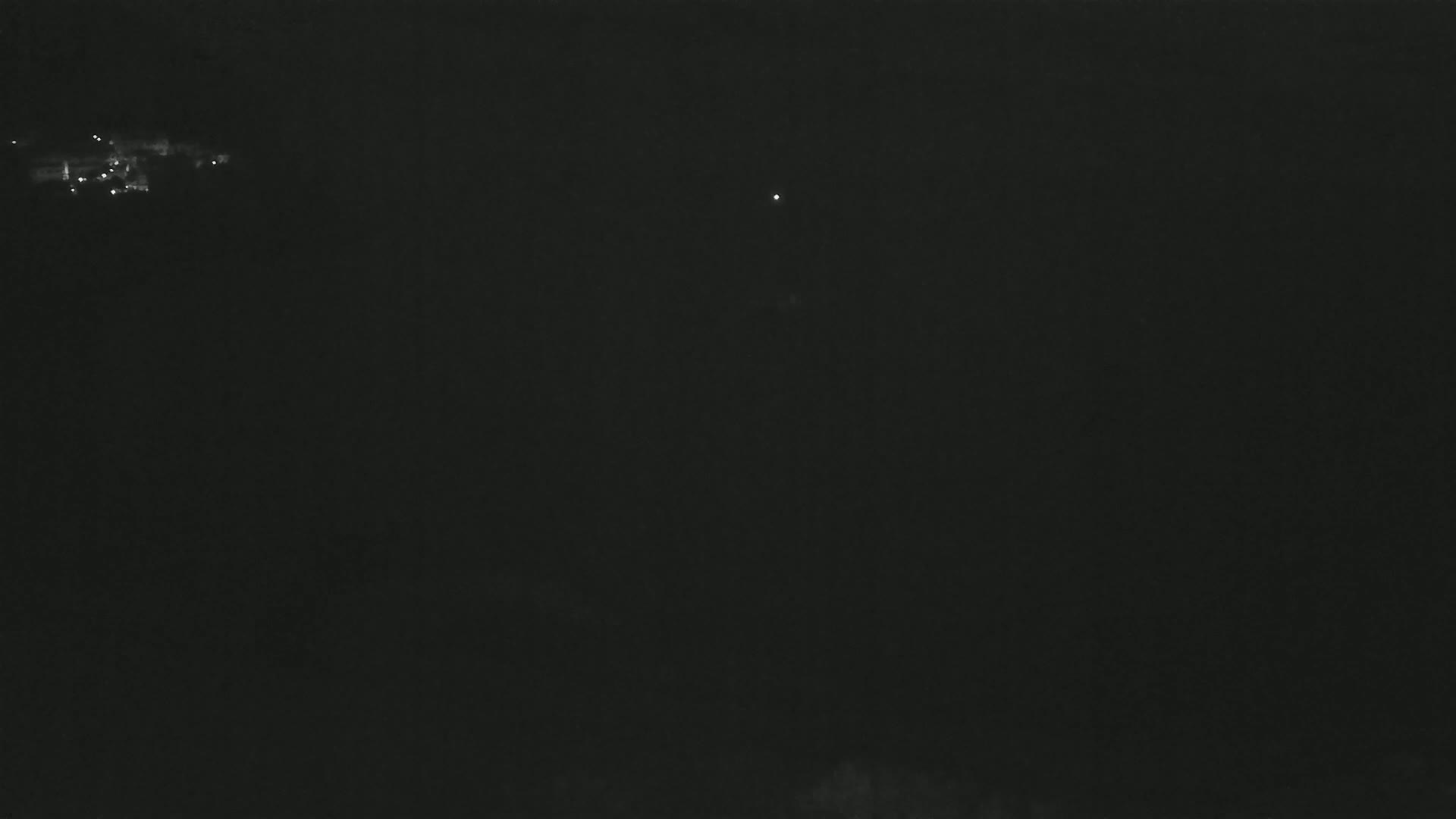 A dark, nighttime scene shows a few faint lights in the distance.