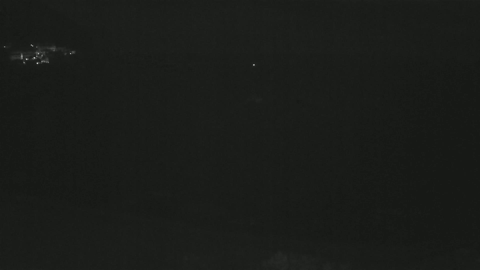 A dark, nighttime scene shows a few faint lights in the distance.
