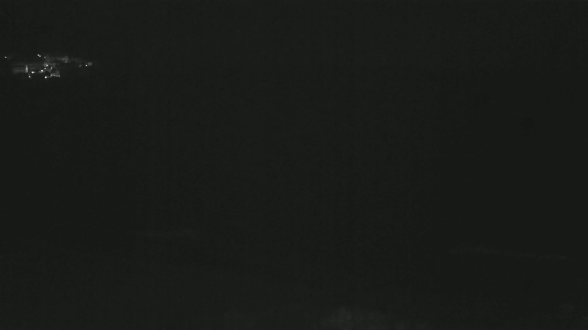 A dark, nighttime scene shows a few faint lights in the distance.