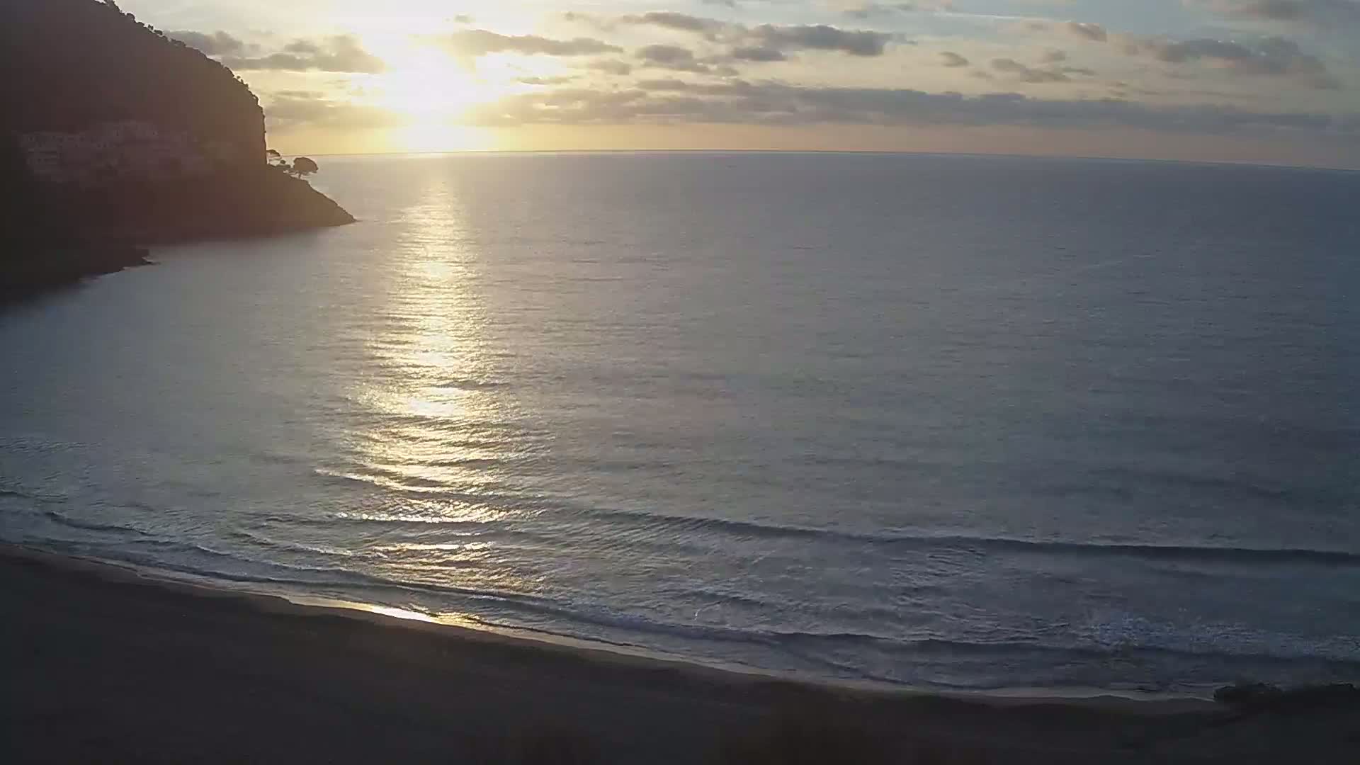 A sandy beach meets a calm ocean under a sunrise sky.