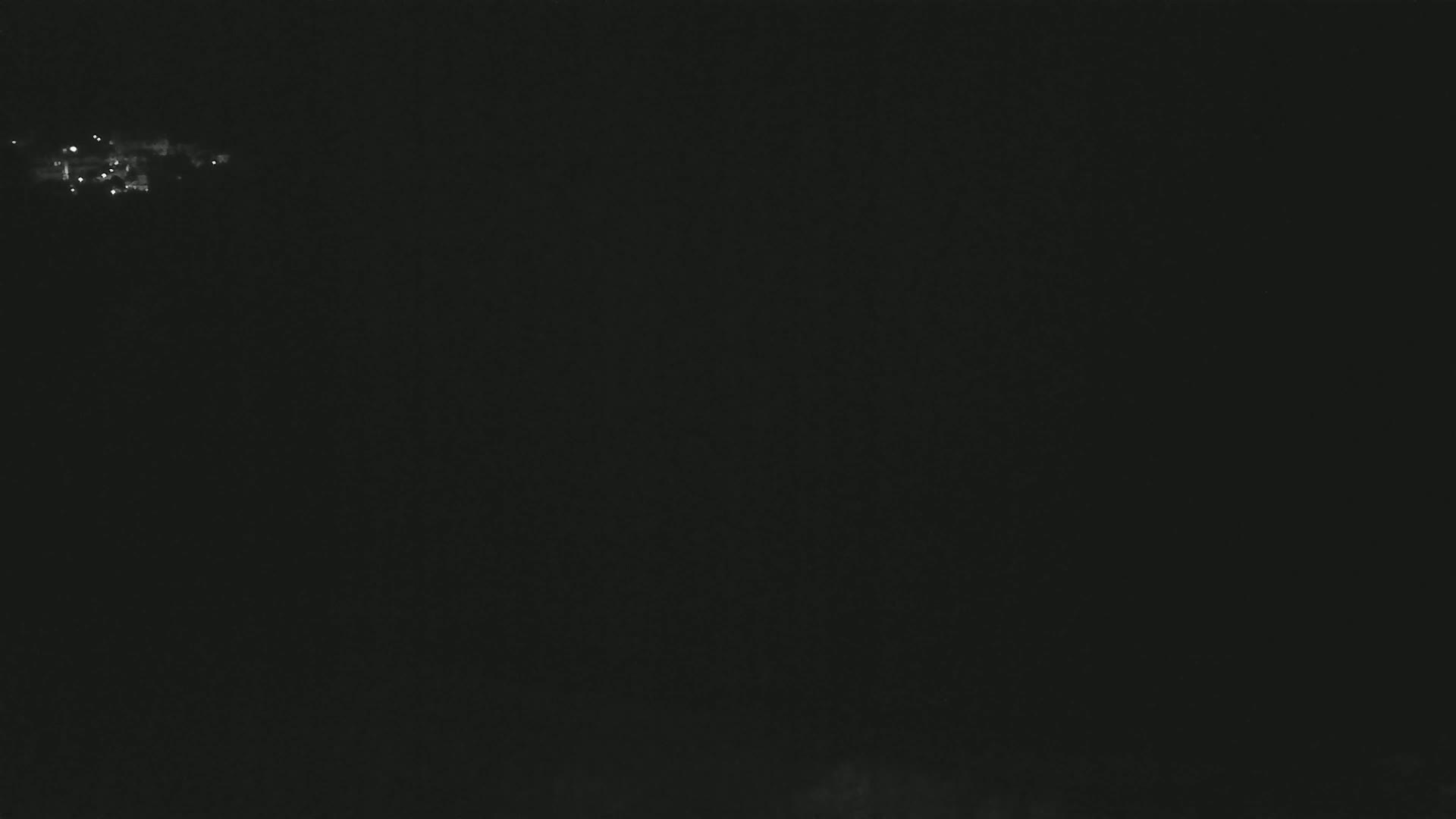A nighttime long shot shows a cluster of faint lights in the distance against a dark, possibly cloudy sky.