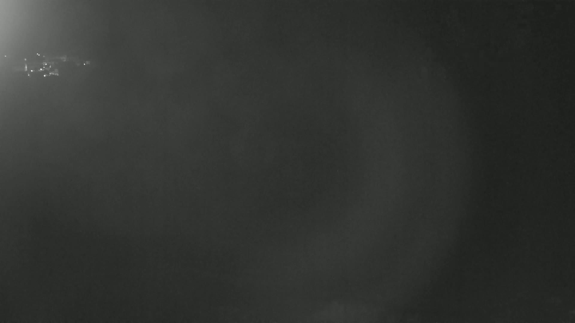A dark, hazy, night scene shows a few distant lights in the far upper left corner.