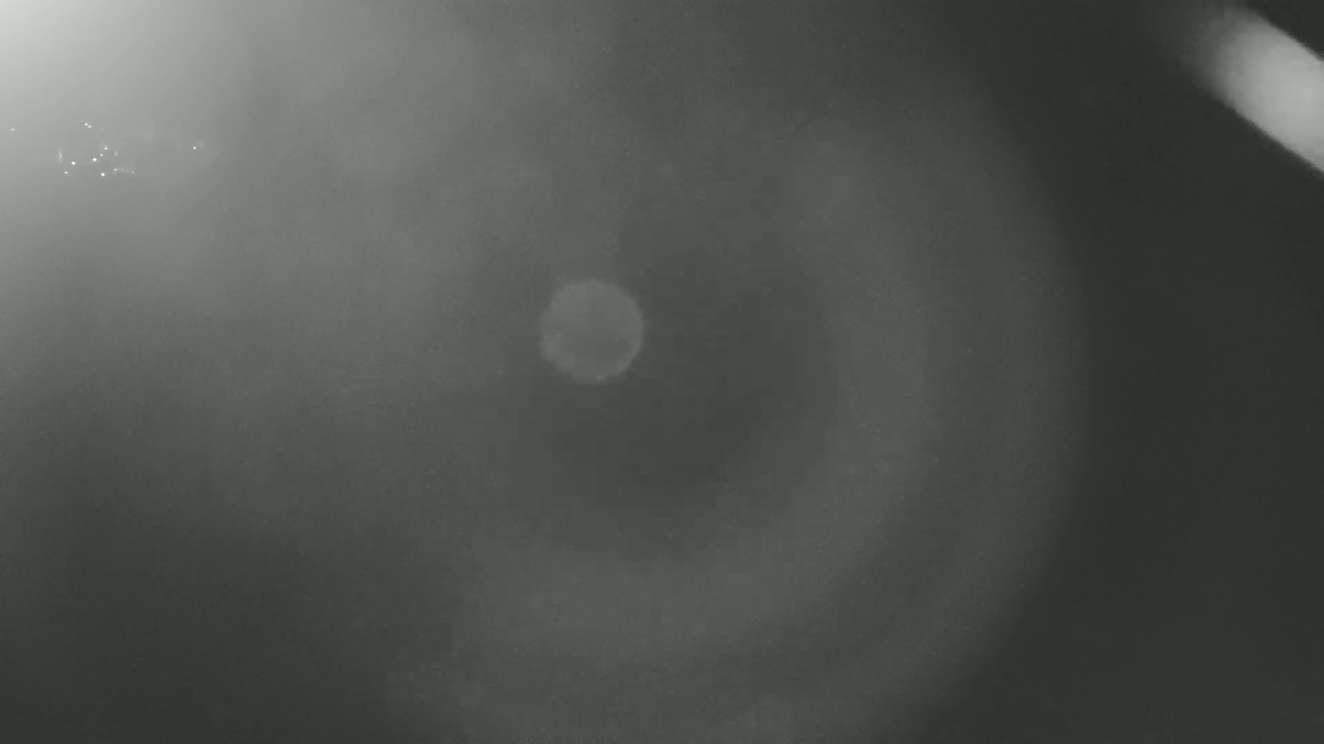 A blurry, hazy grayscale image shows a pale circle in the center, possibly a light source, surrounded by a darker, swirling, opaque atmosphere.