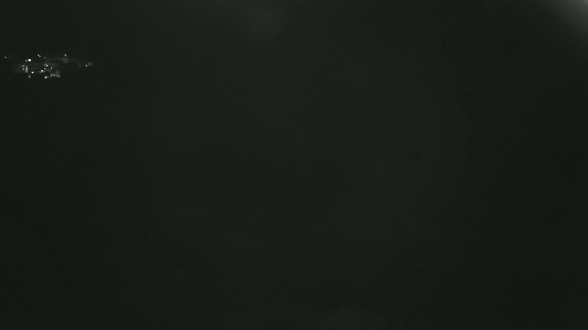A dark, nighttime scene shows a few faint lights in the distance.