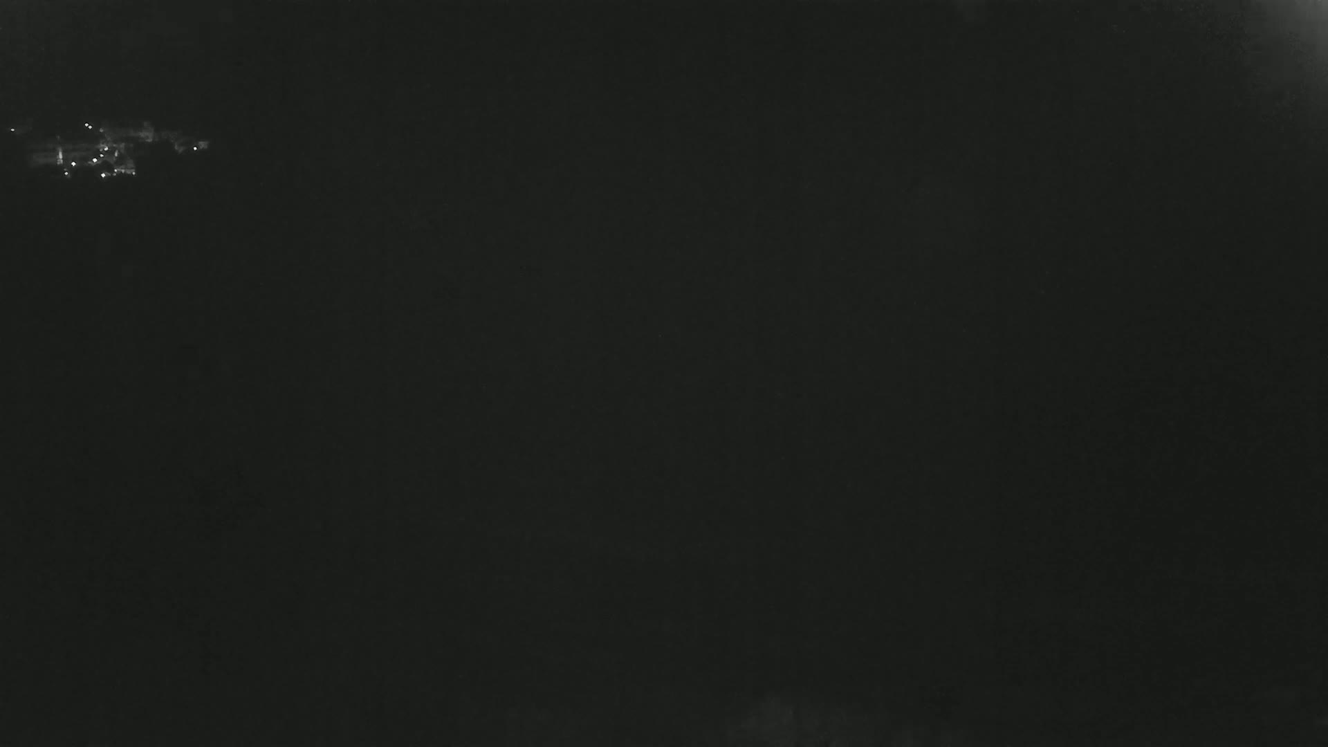 A dark, nighttime scene shows a small cluster of distant lights on the horizon.