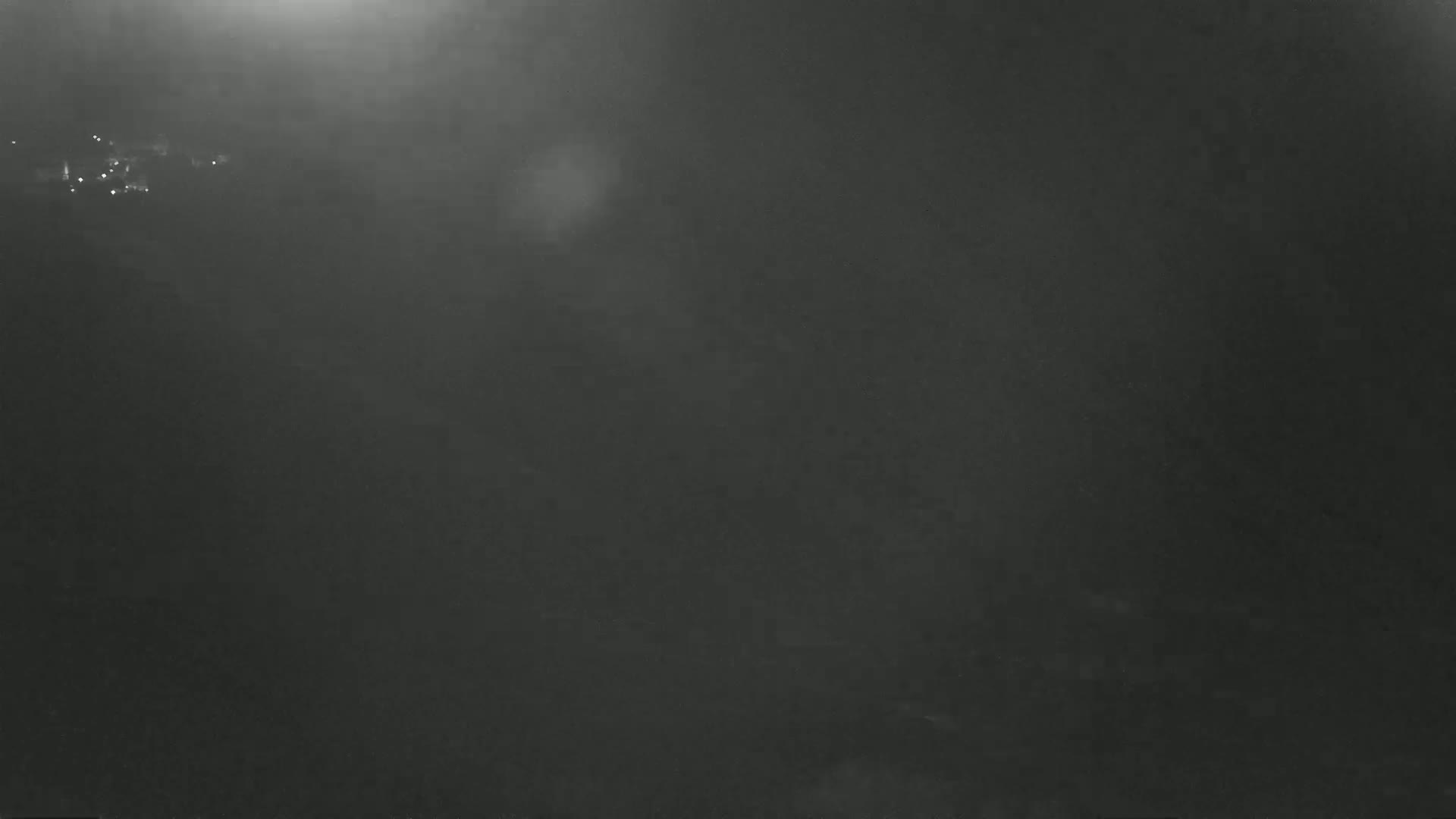 A dark, hazy scene shows a few faint lights in the distance under a foggy or smoky sky.
