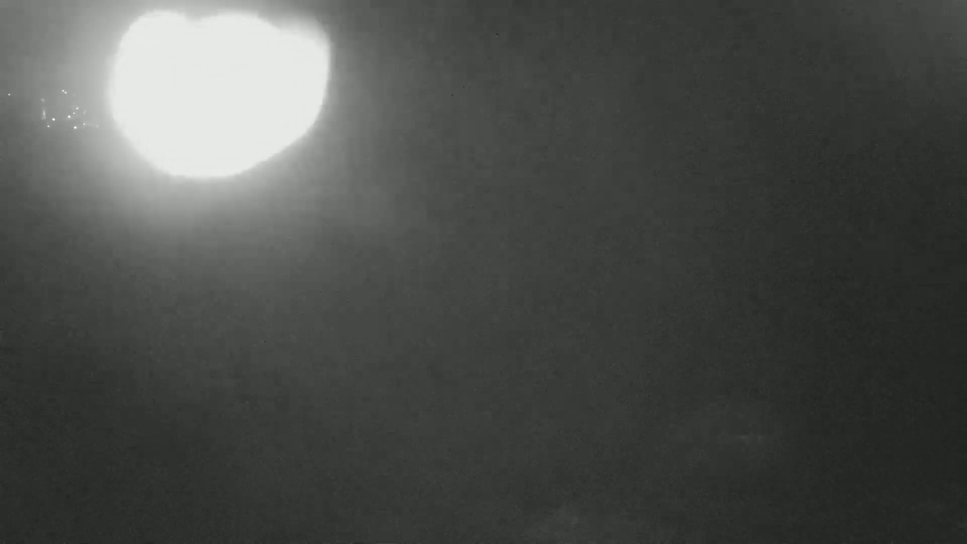 A bright light source illuminates a dark, hazy sky.