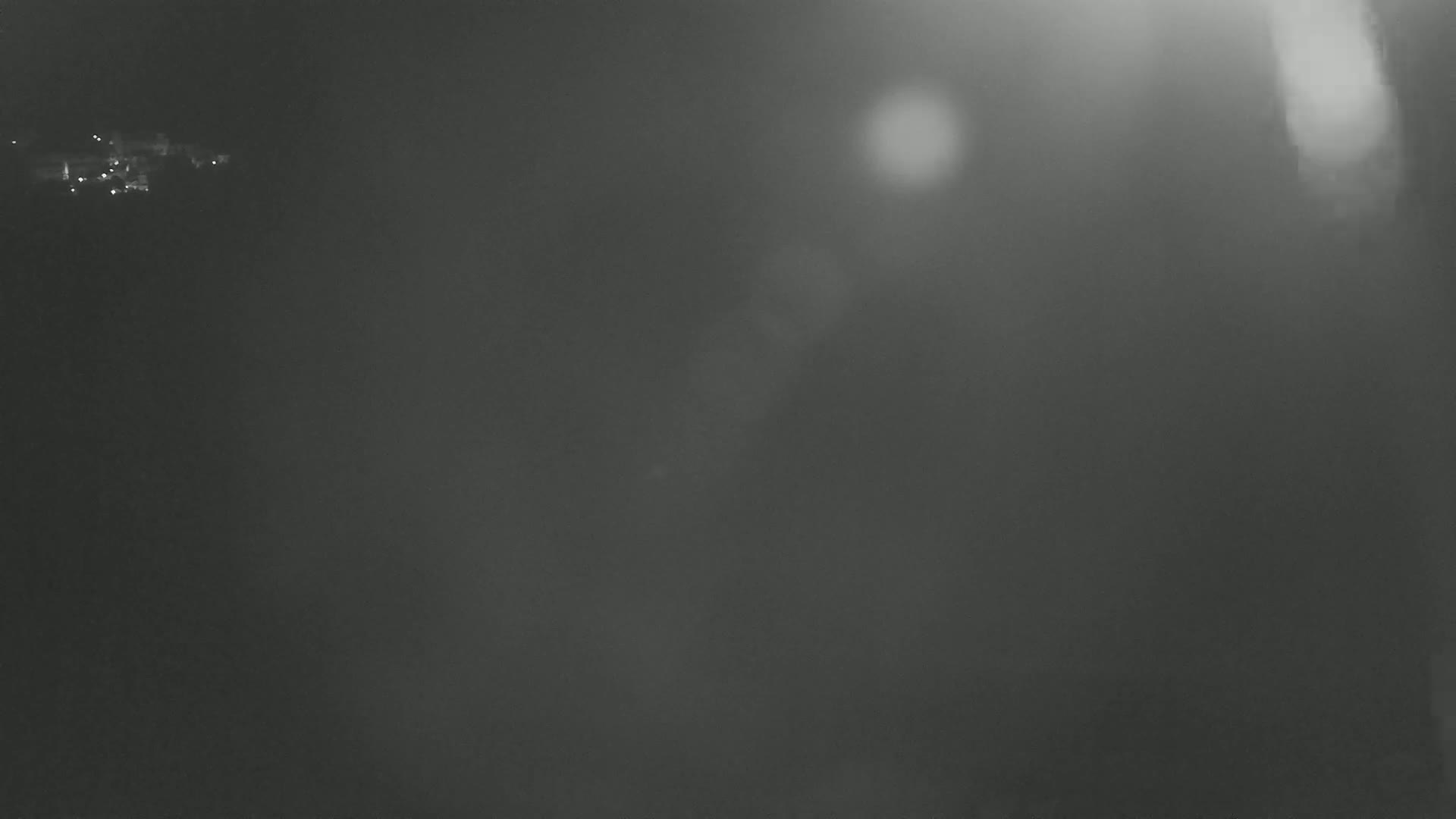 A blurry, dark gray image shows a hazy, possibly foggy, night scene with distant, indistinct lights.