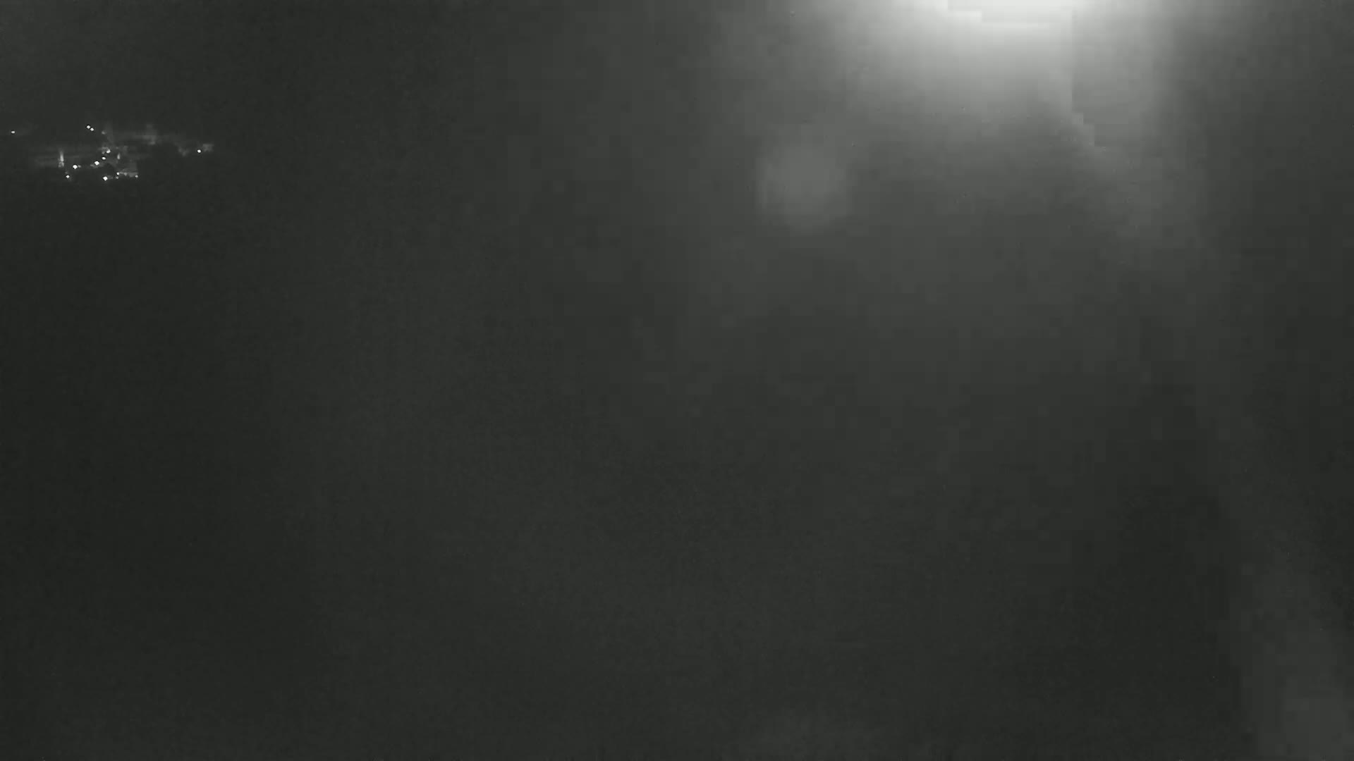 A dark, hazy nighttime scene shows a few distant lights in the upper left corner and a bright light source in the upper right, obscuring most of the view.