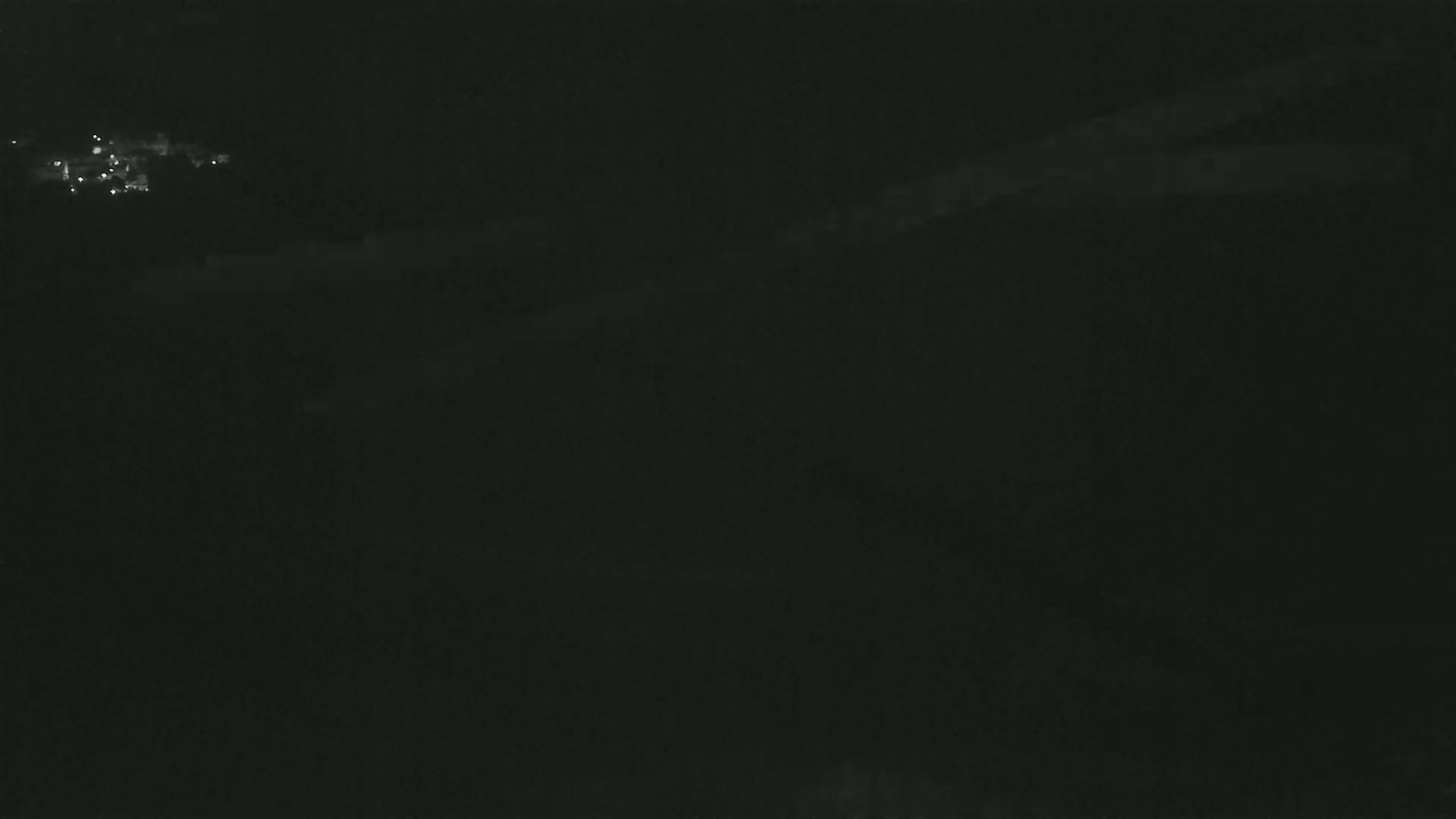 A dark, nighttime scene shows a faint cluster of lights in the distance under a mostly clear, dark sky.