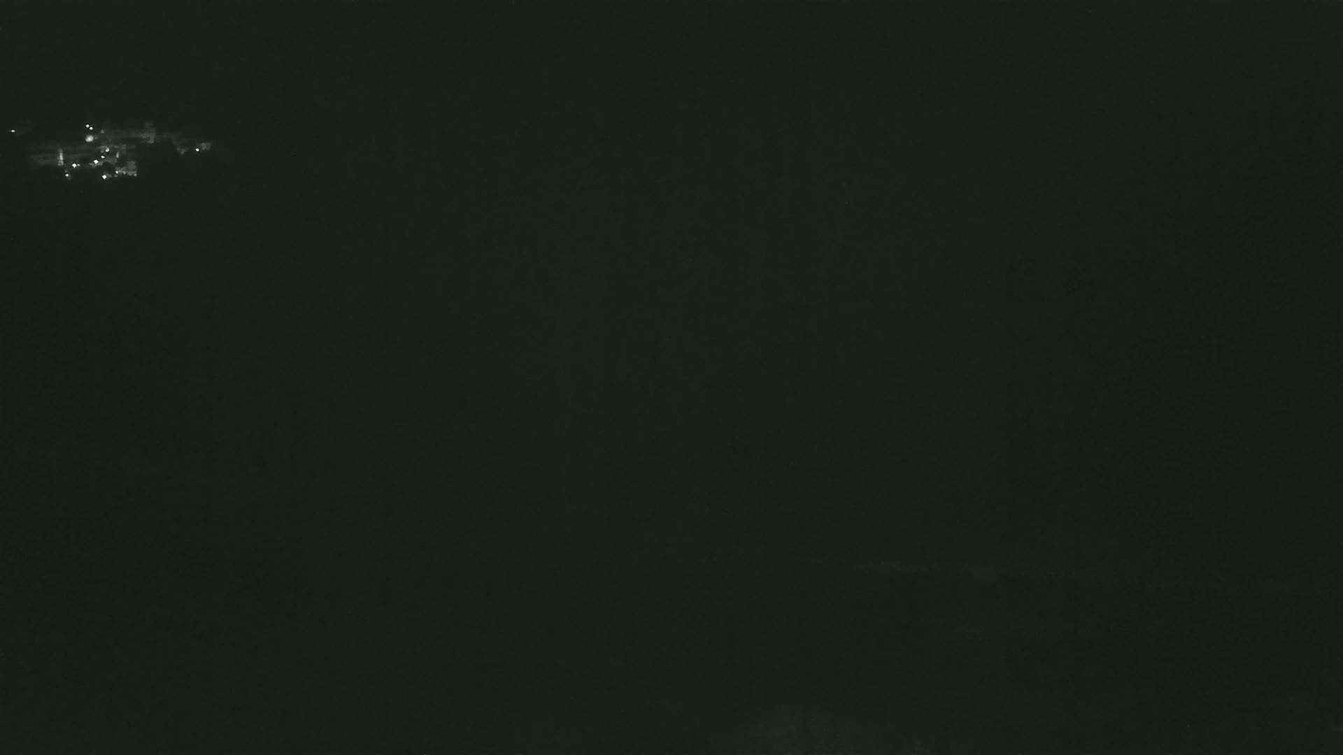 A dark, nighttime scene shows a small cluster of faint lights in the distance.