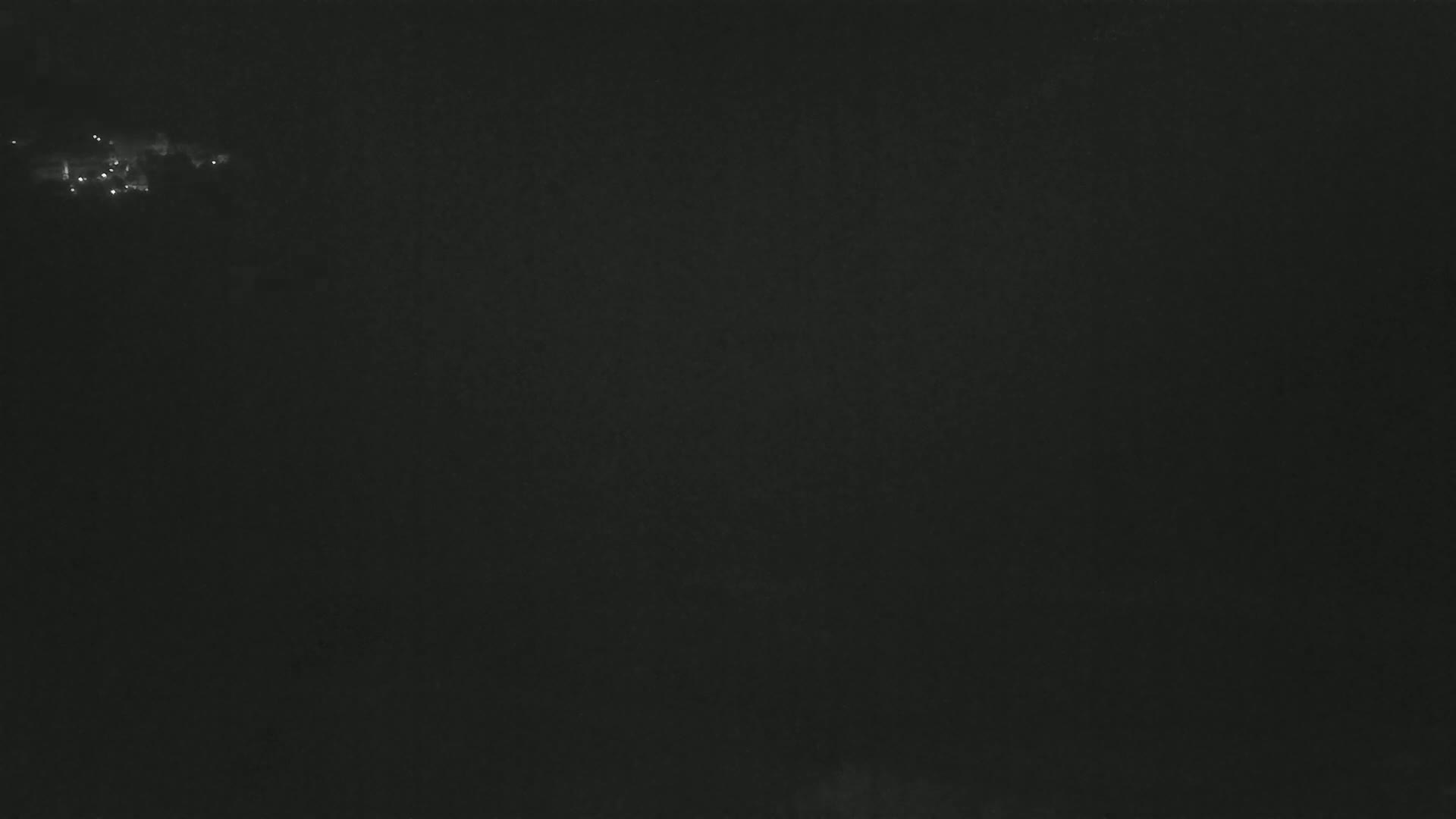 A dark, nighttime scene shows a small cluster of faint lights in the distance.