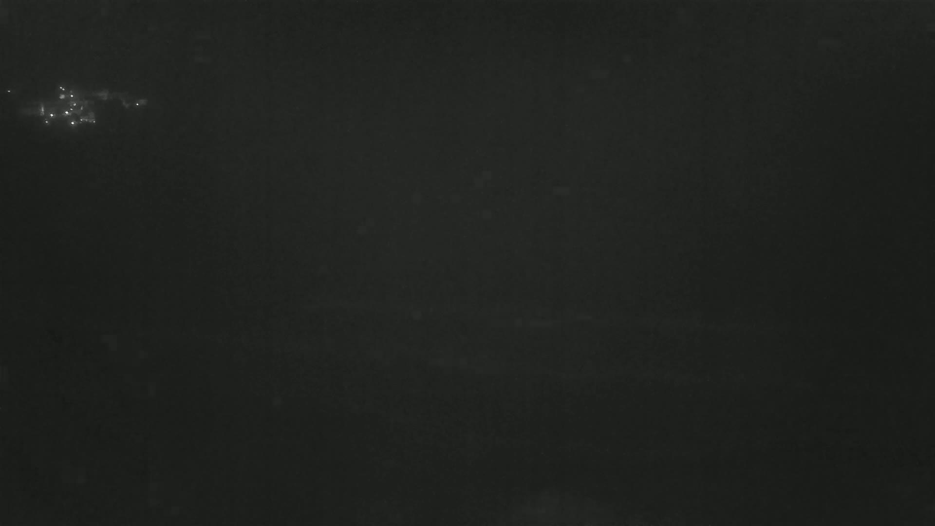 A dark, nighttime scene shows a cluster of faint, distant lights against a mostly black background.