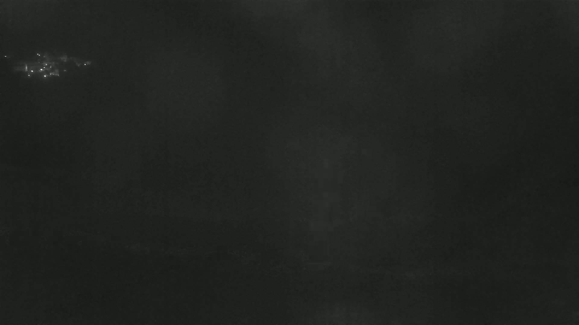 A dark, foggy night scene shows a few faint lights in the distance.