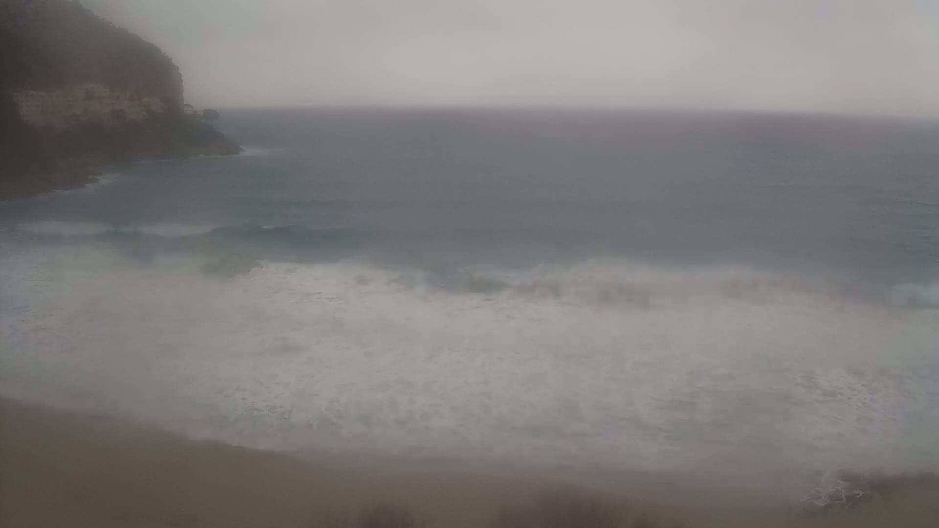 A hazy, overcast day shows a rocky cliff overlooking a beach with waves crashing on the shore.
