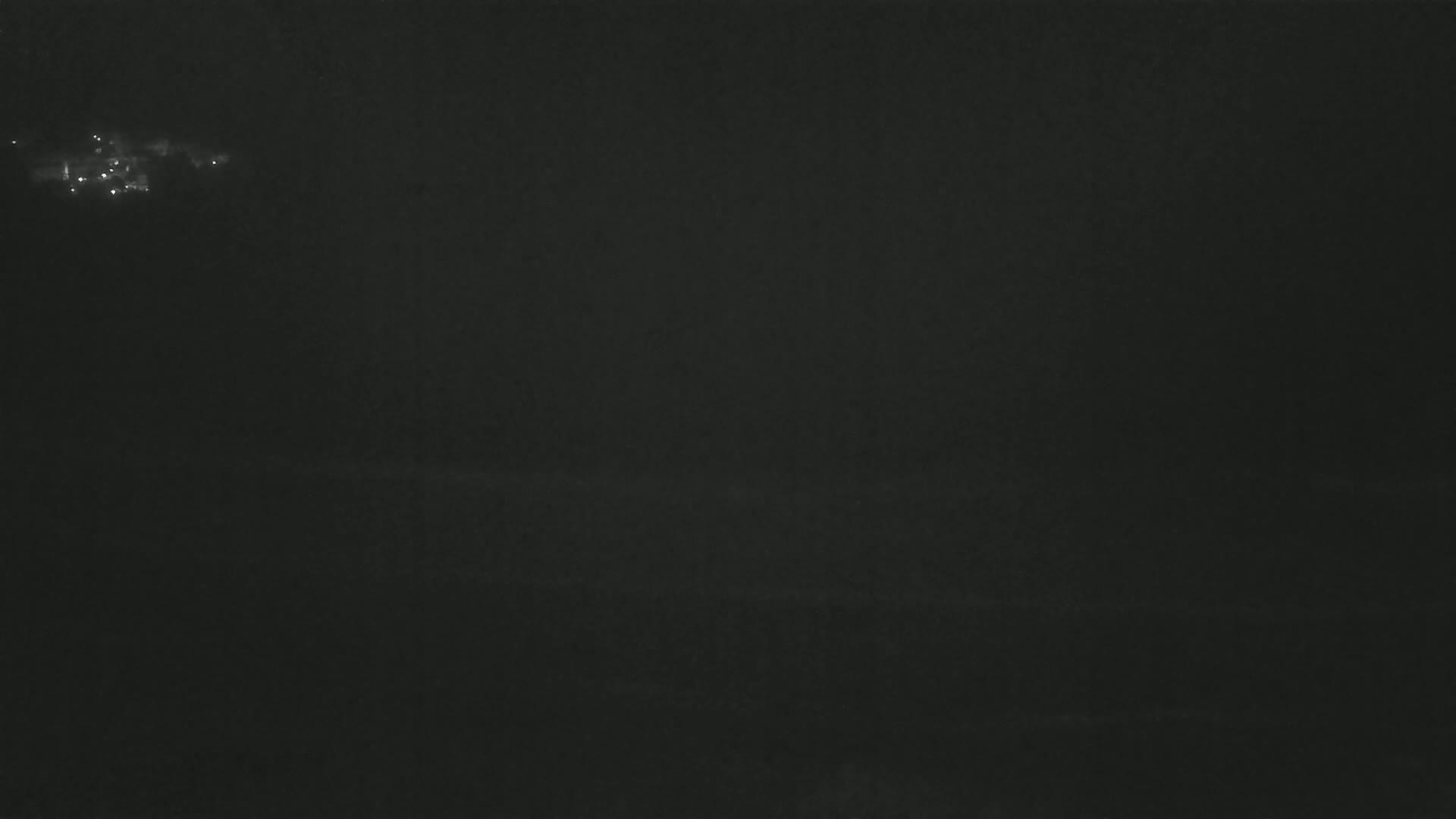 A dark, nighttime scene shows a cluster of faint lights in the distance.