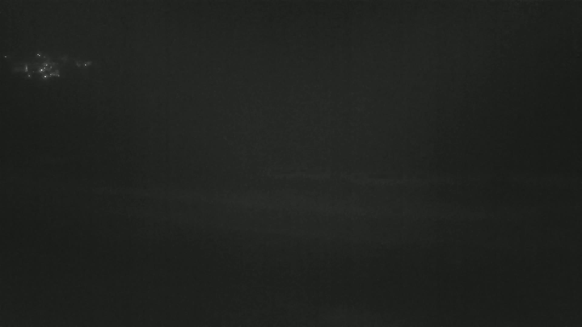 A dark, nighttime scene shows faintly illuminated points of light in the distance under a hazy sky.