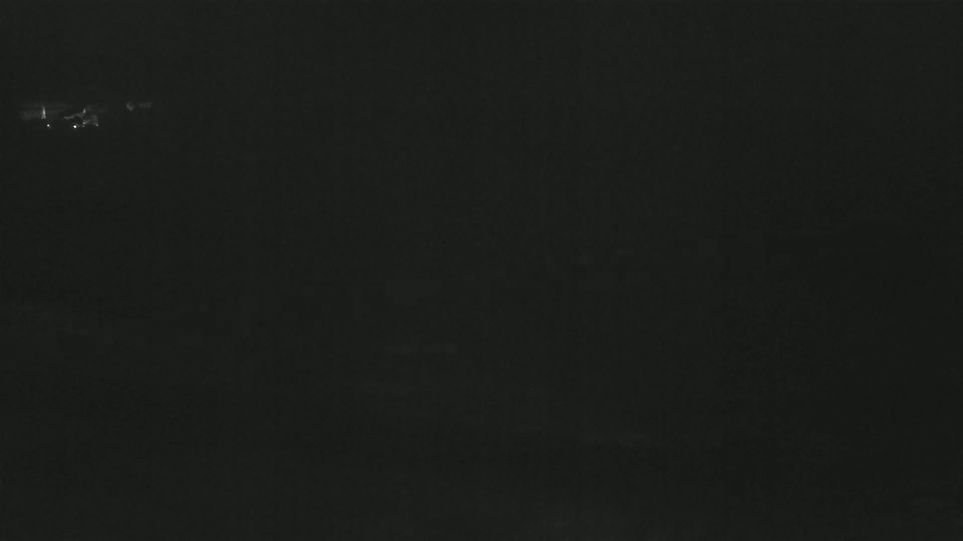 A dark, nighttime image shows a few faint lights in the far distance.