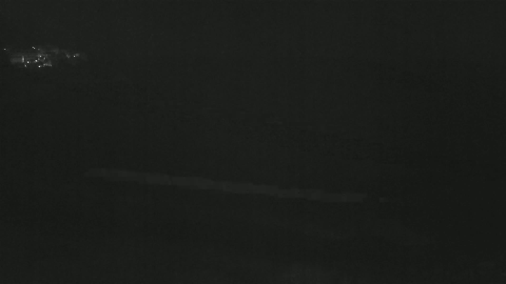 A dark, nighttime scene shows a faint line of lights in the distance and a darker area possibly representing water or land in the middle ground.