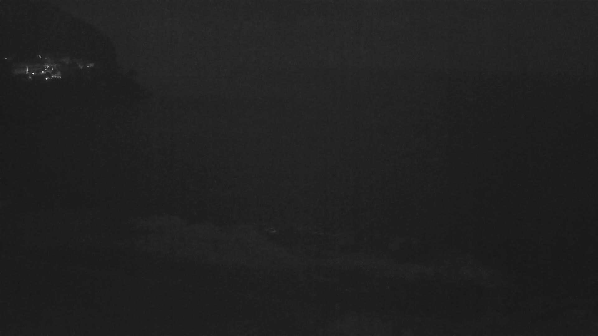 A dark, nighttime scene shows a hazy or foggy landscape with faint lights visible in the distance.