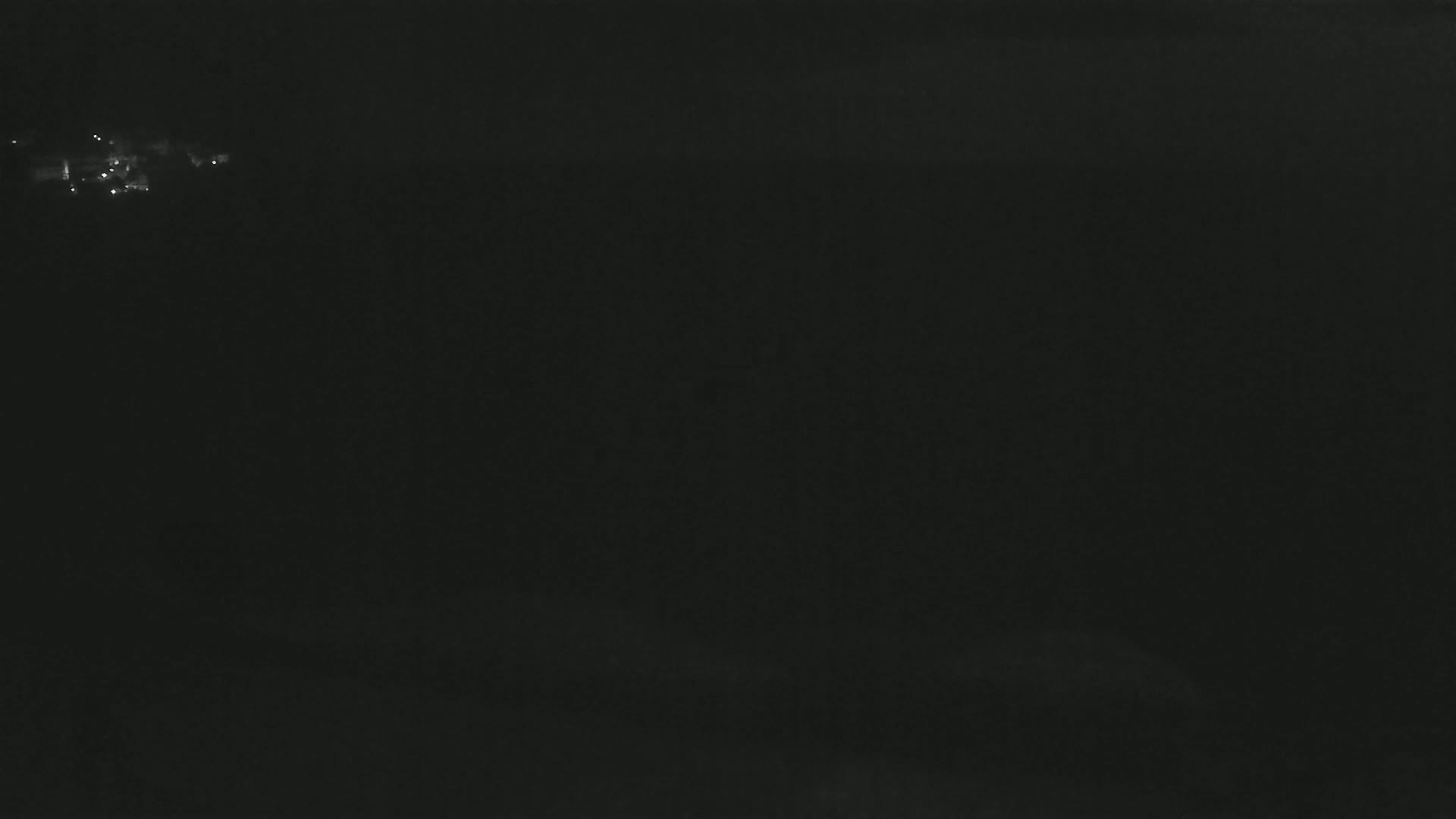 A dark, nighttime scene shows a few faint lights in the distance.