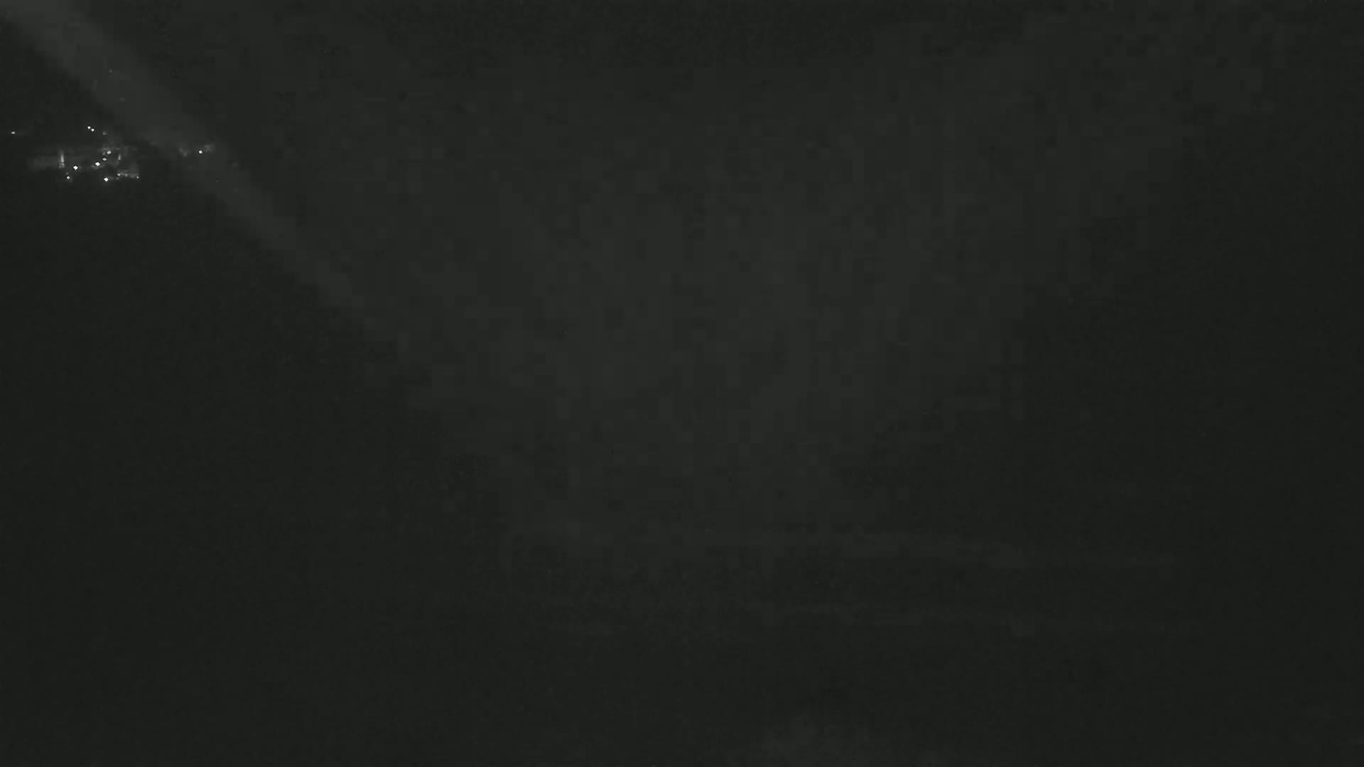 A dark, nighttime scene shows a few faint lights in the distance, possibly from a town or city, illuminated by a bright beam of light from above.