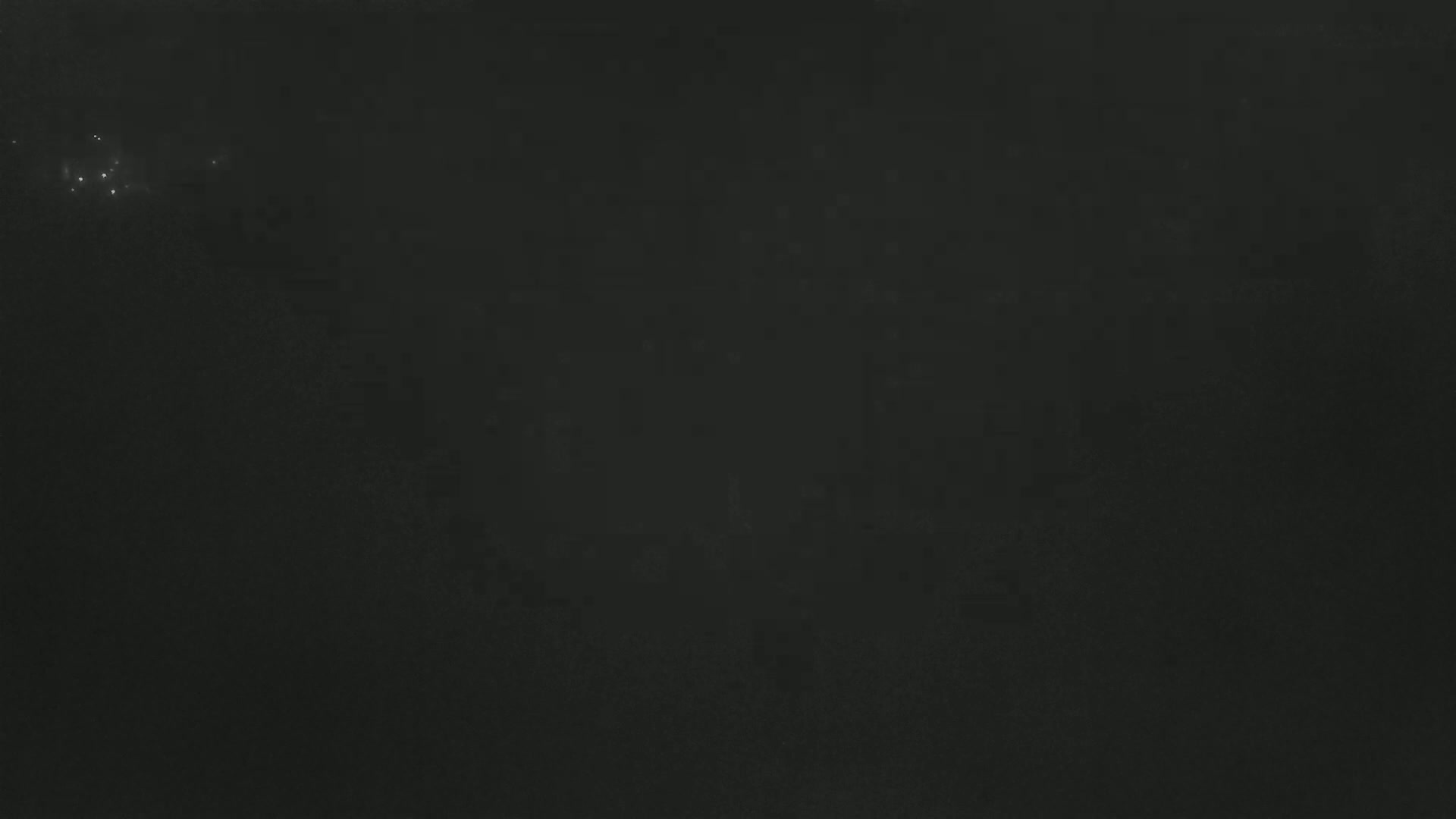 A dark, possibly nighttime image shows a few faint, distant lights in a hazy or foggy atmosphere.