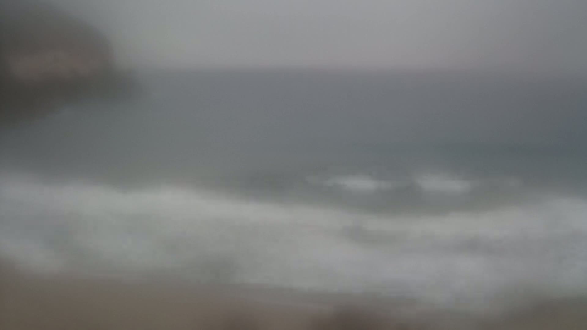 A blurry view of a grey, overcast ocean with small waves breaking near a shore.