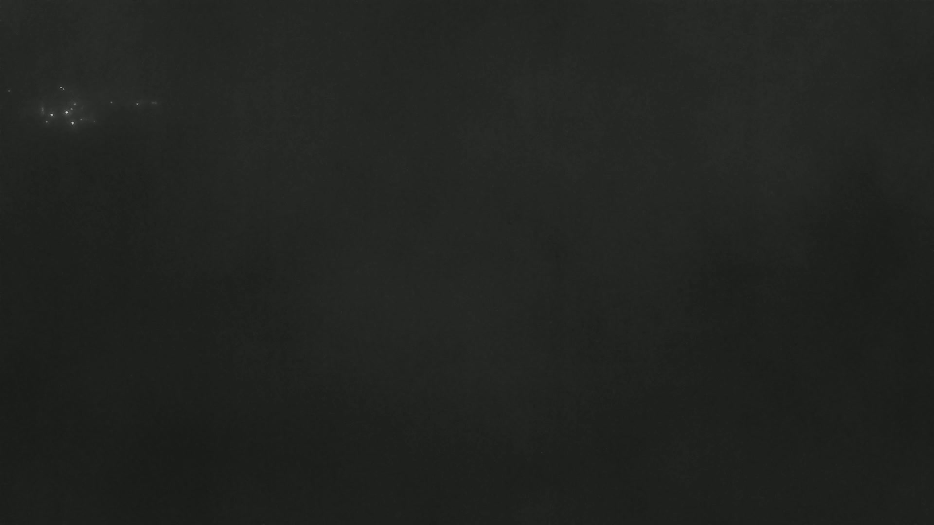 A dark, possibly nighttime, scene shows a few faint lights in the distance against a mostly dark, textured background.