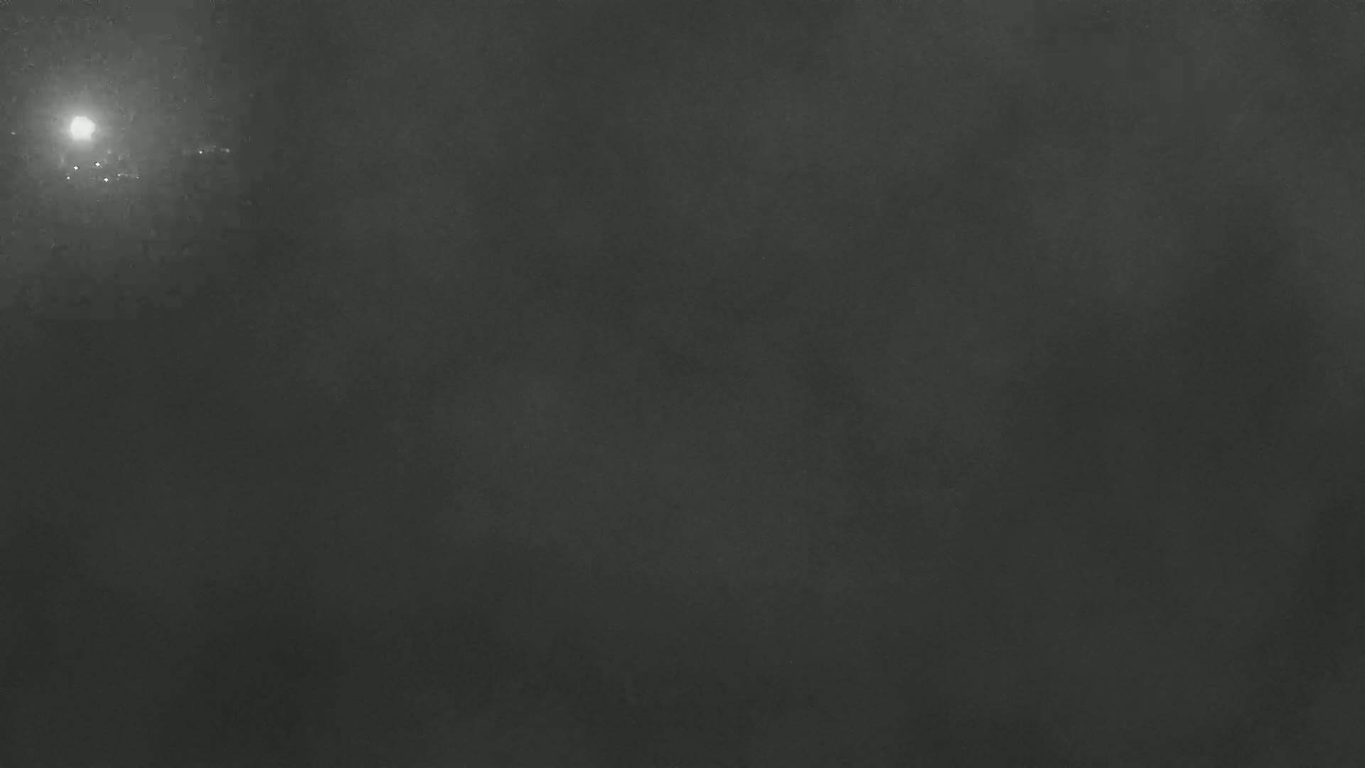 A blurry, dark gray image shows a bright light in the upper left corner on a hazy or foggy night.