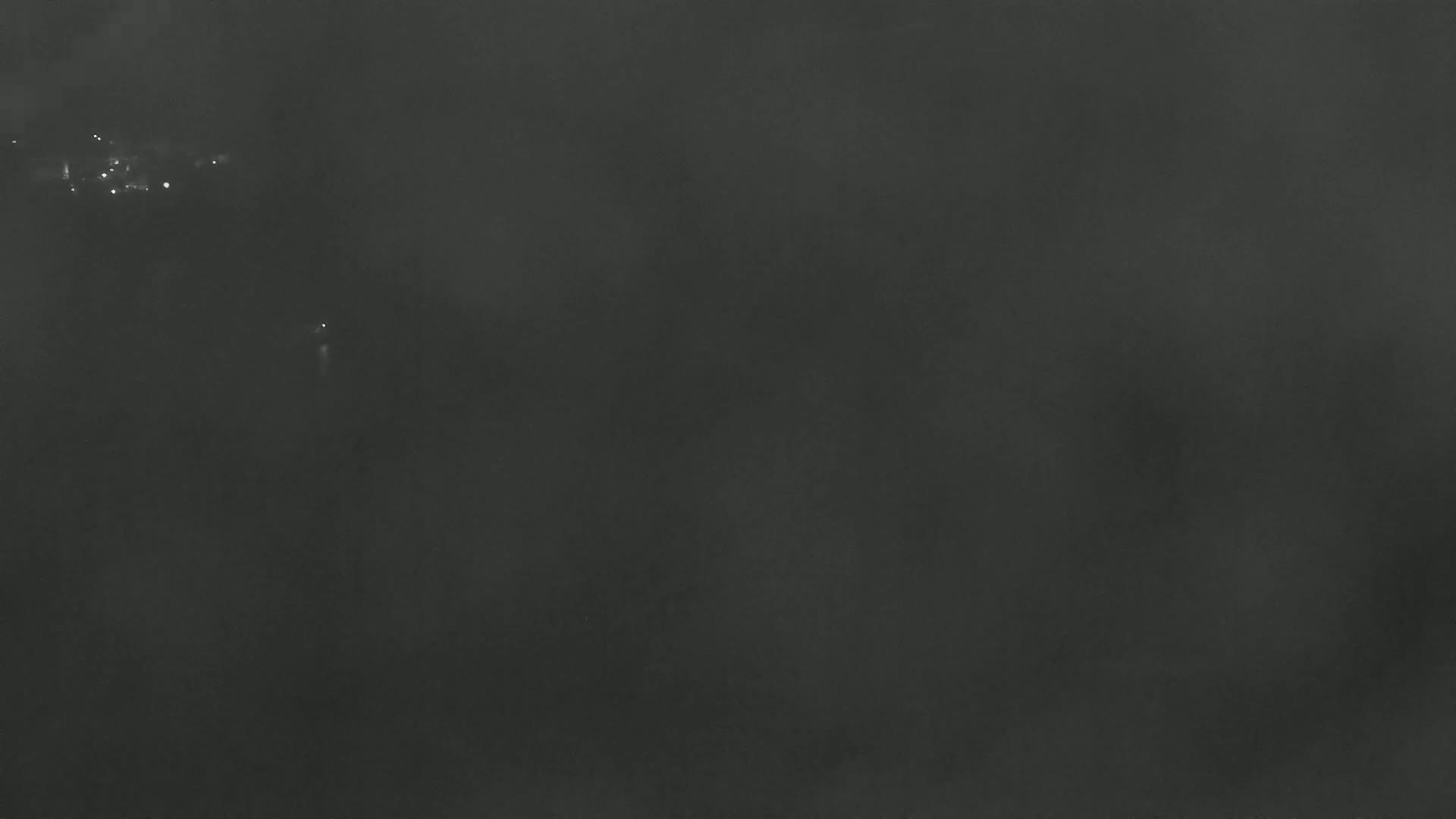 A dark, foggy landscape is visible at night with a few distant lights.