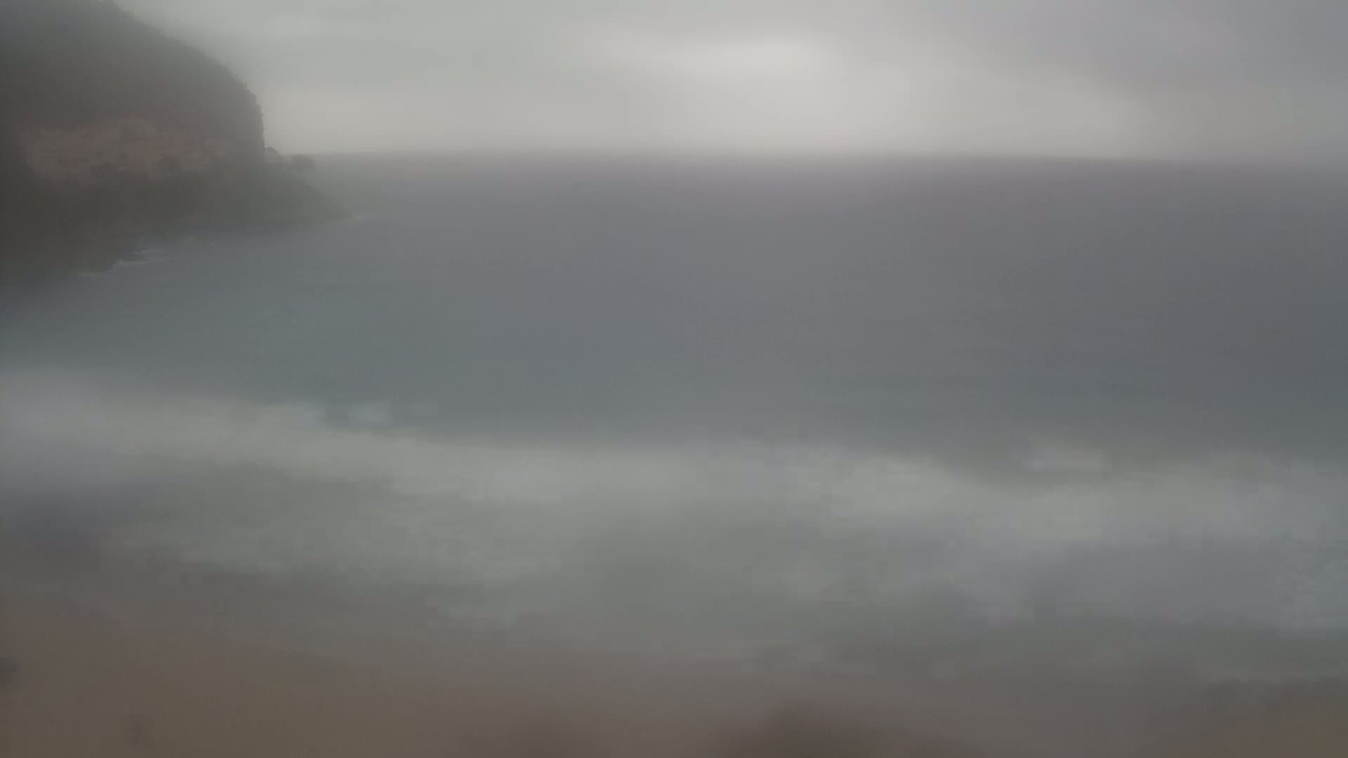 A hazy, overcast day shows a rocky cliff overlooking a sea with small waves.