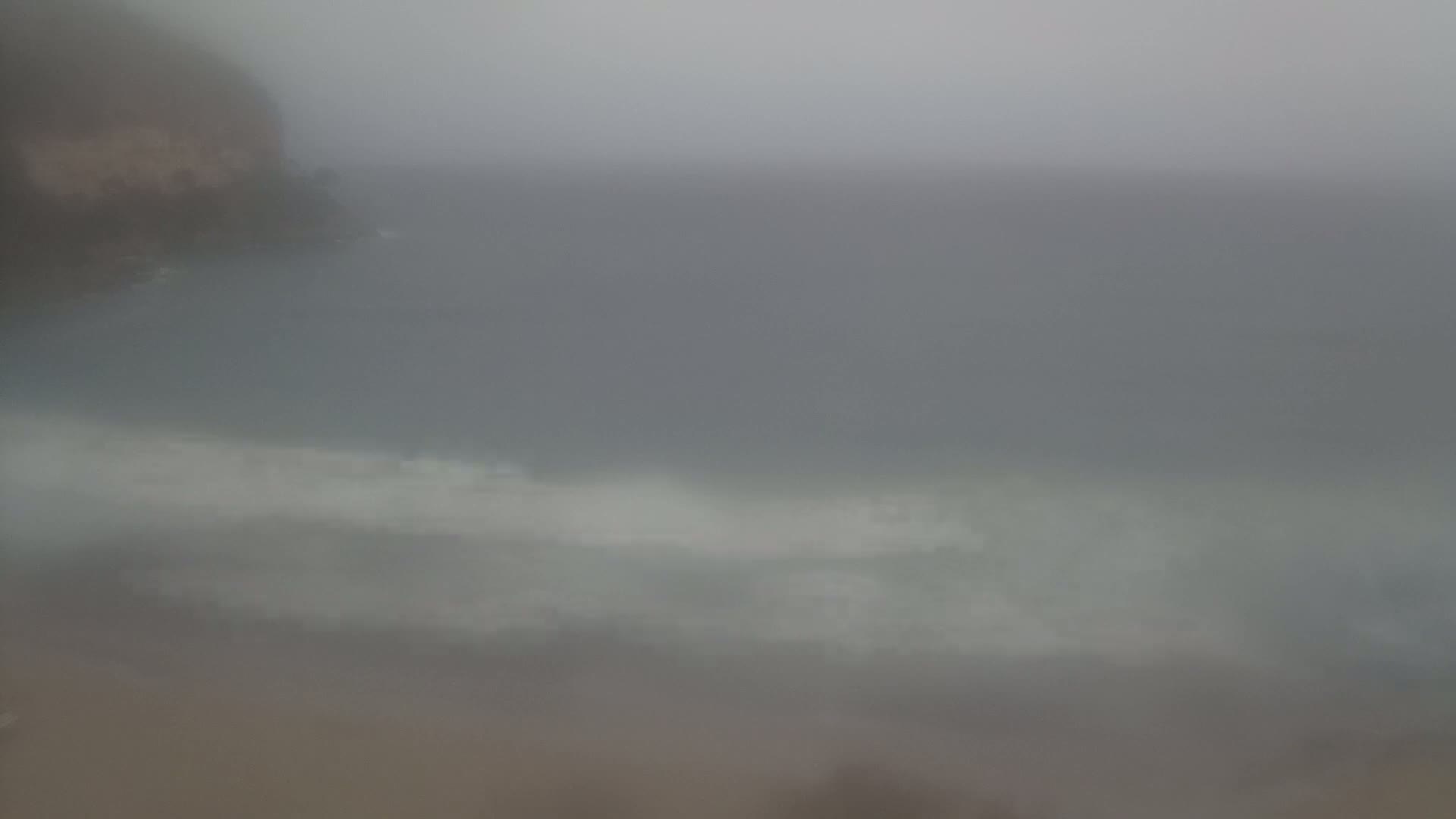 A hazy, overcast day shows a blurry view of a rocky shoreline and ocean waves.