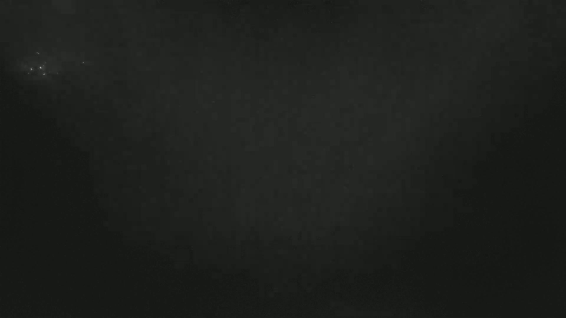 A mostly dark image shows a few faint, bright specks in the upper left corner against a dark, textured background.