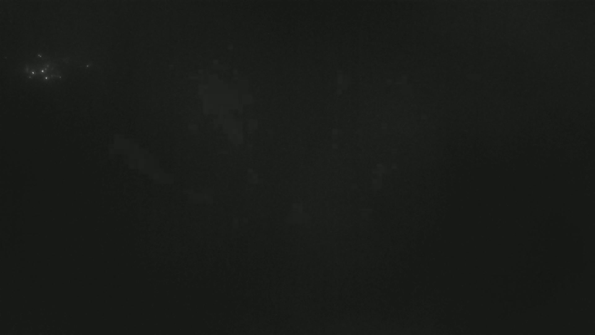A dark night sky shows faint, blurry light sources and a few brighter lights clustered together in the upper left corner.