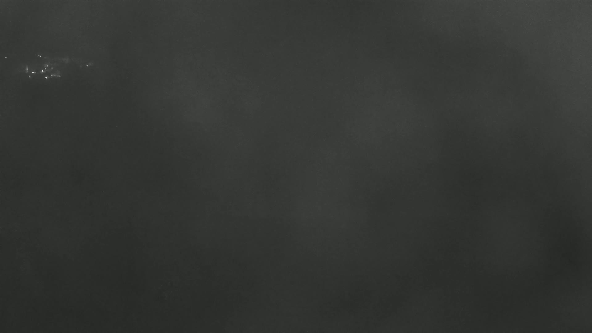 A dark, possibly foggy or hazy, nighttime scene with a few faint lights in the distance.