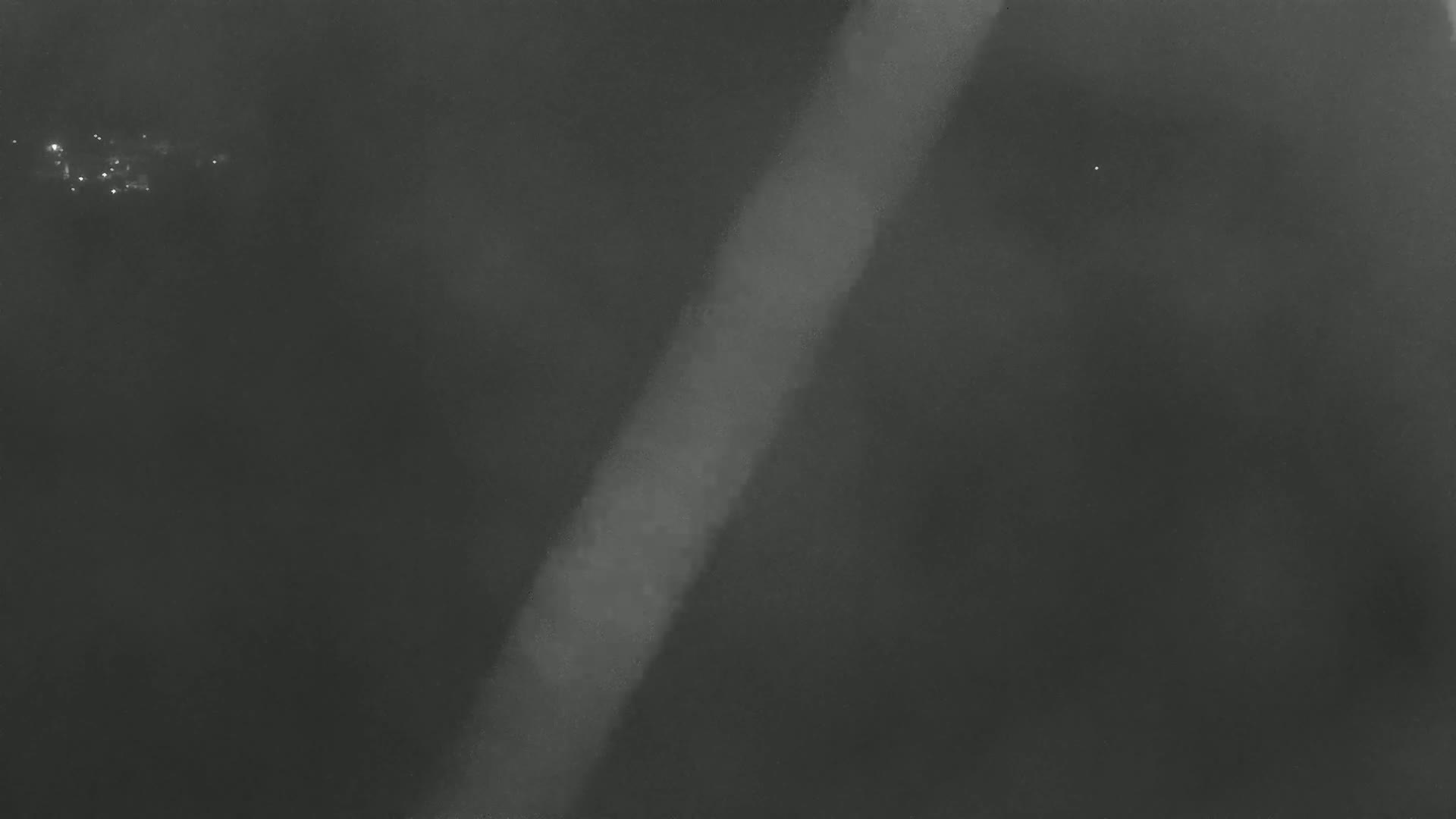 A bright, vertical streak of light cuts diagonally across a dark, hazy, nighttime sky.