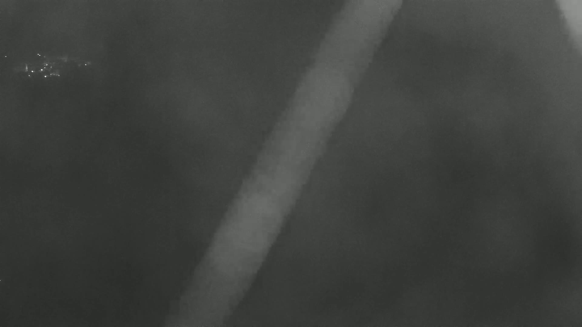 A blurry, grayscale image shows a diagonal, lighter-colored streak against a dark, hazy background.