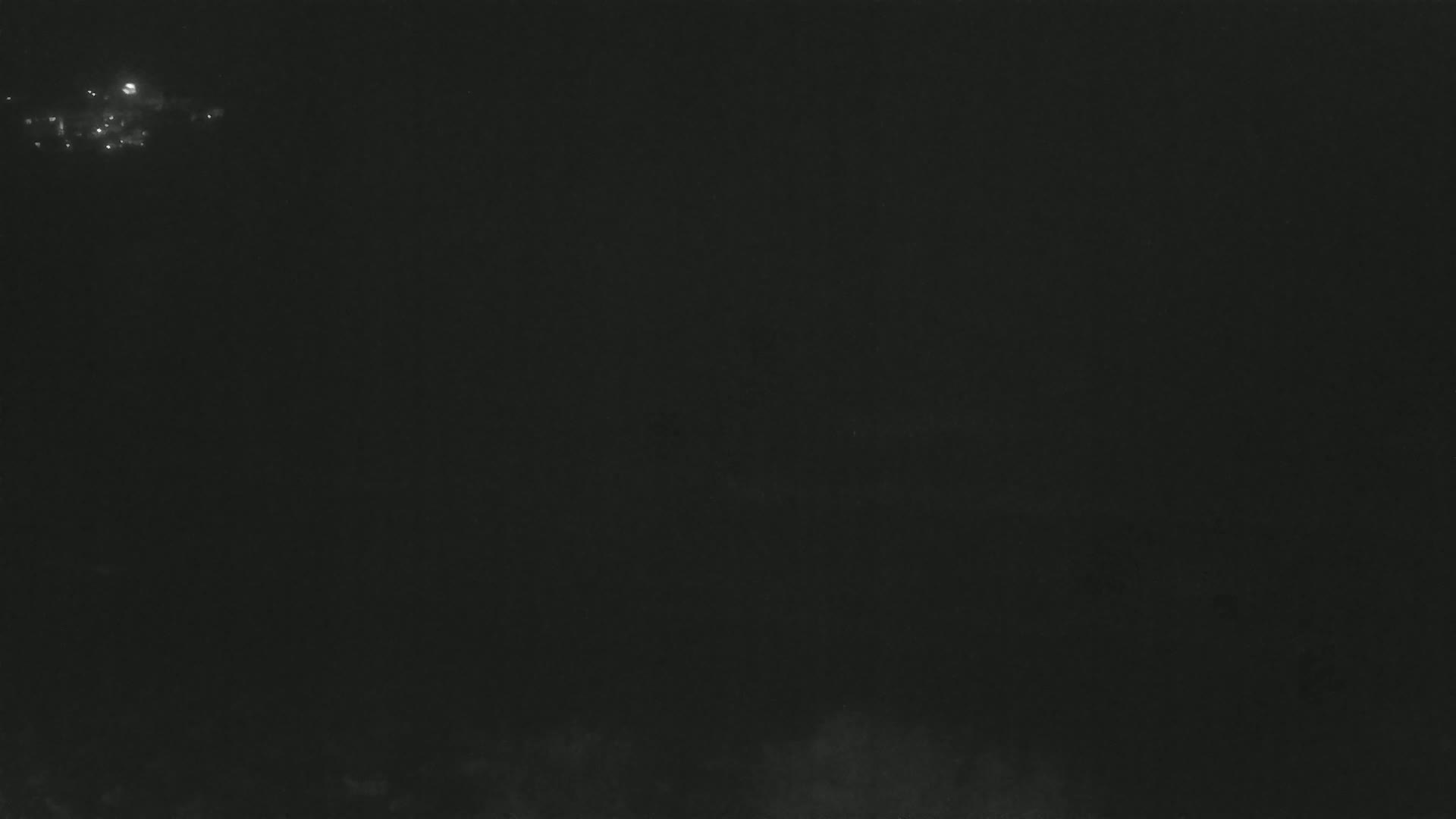 A dark, nighttime scene shows a few faint lights in the distance and some hazy cloud or mist near the bottom.