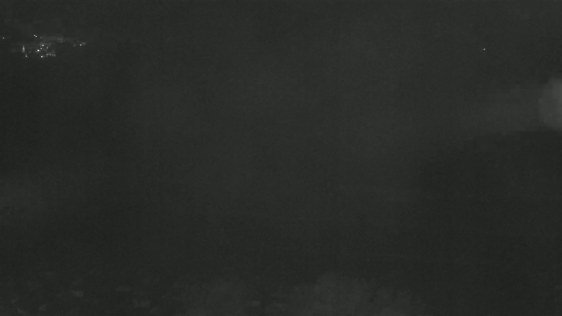 A dark, nighttime scene shows a few faint lights in the distance under a hazy sky.