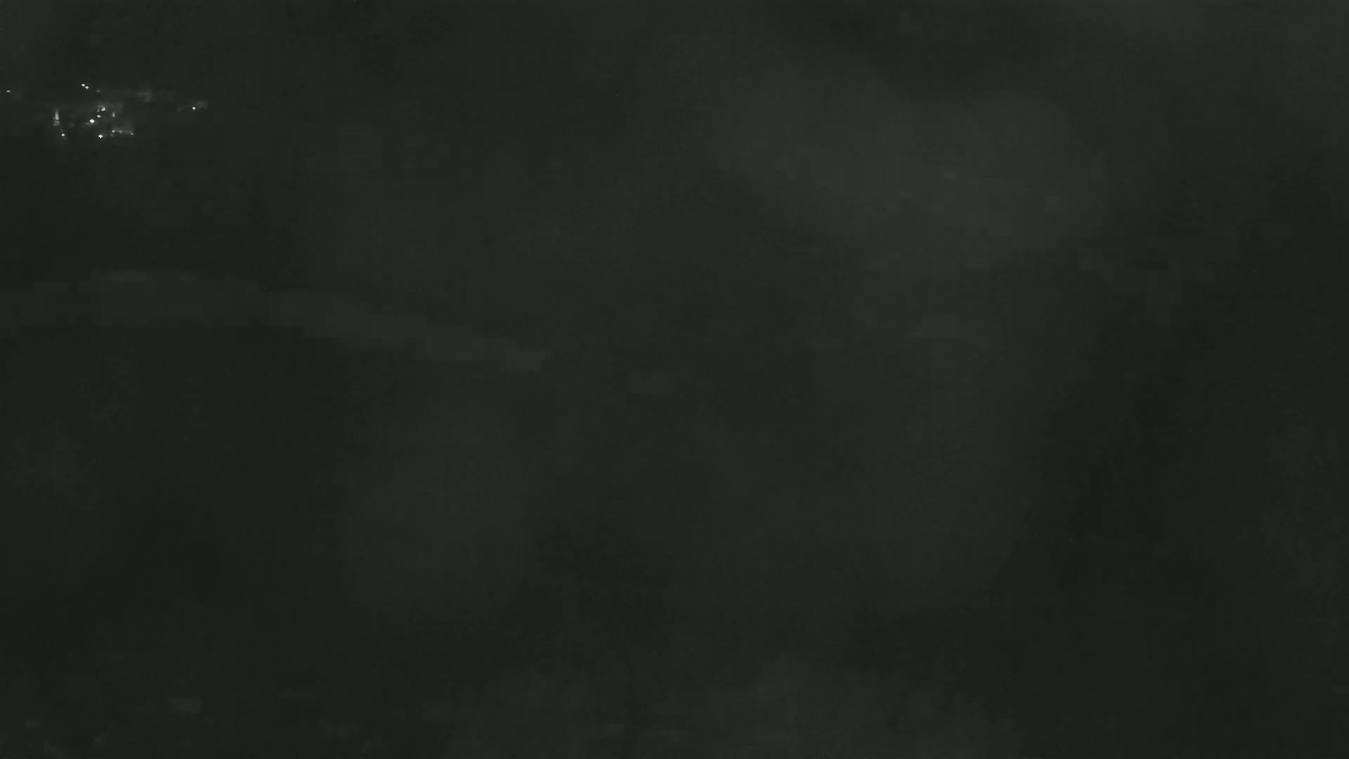 A dark, possibly nighttime, image shows a blurry, indistinct scene with faint lights in the distance.