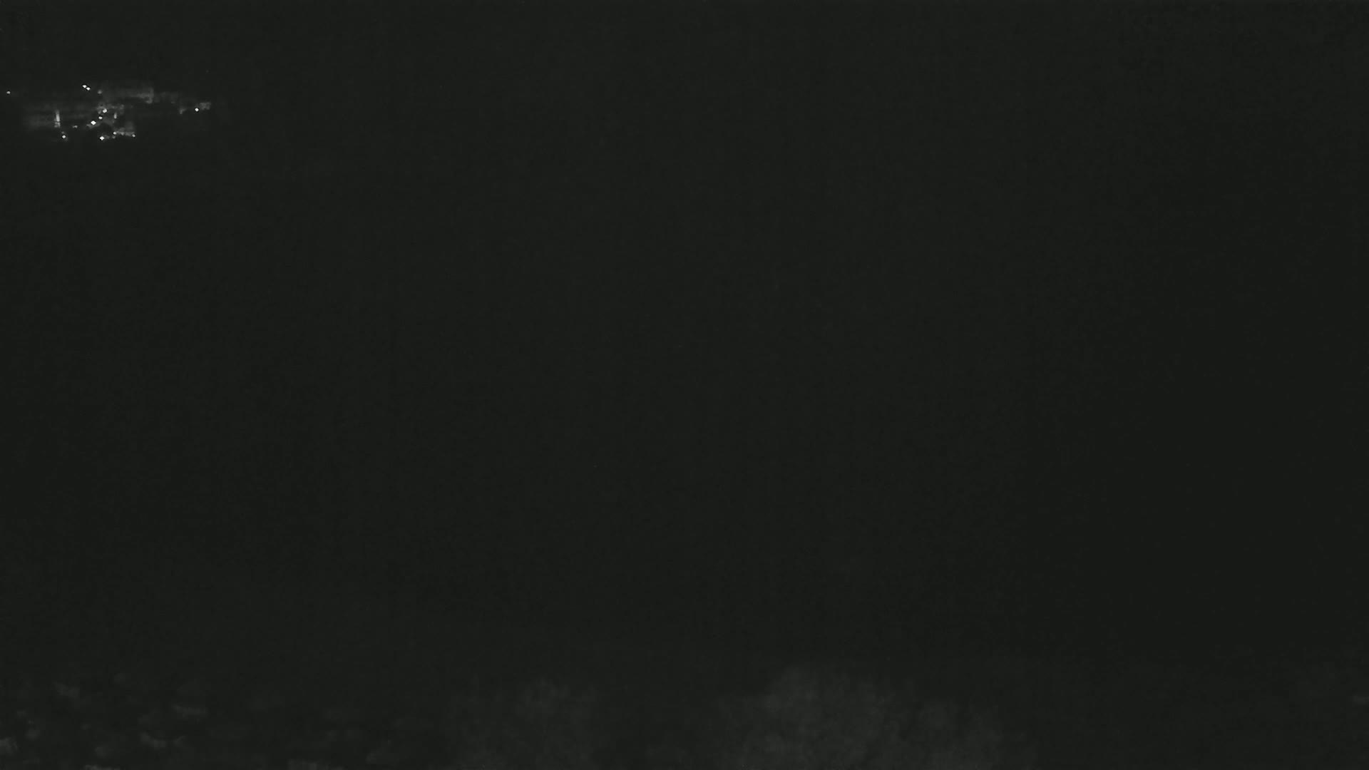 A dark, nighttime scene shows a few faint lights in the distance.