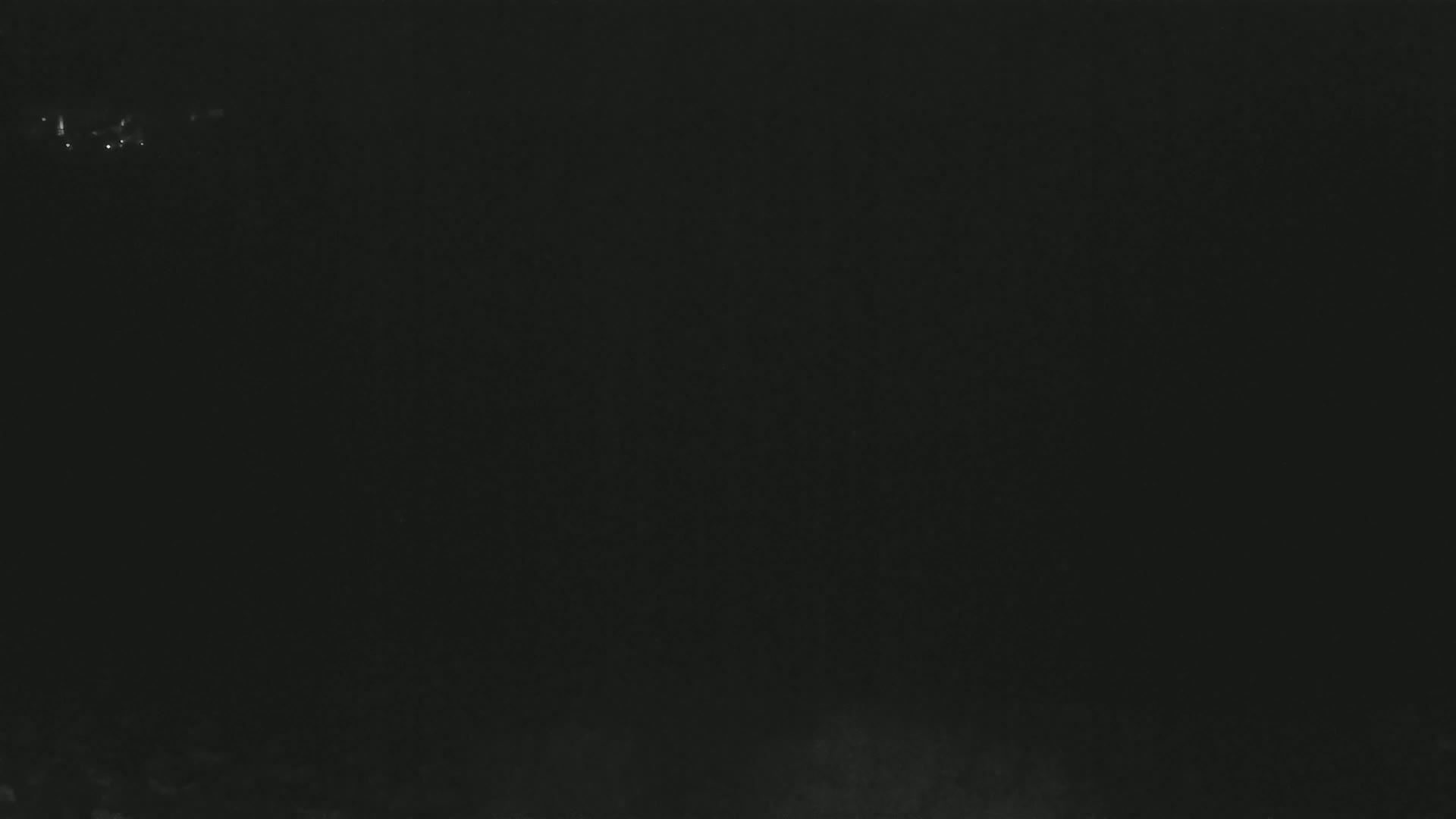 A dark, nighttime scene shows a few faint lights in the distance.