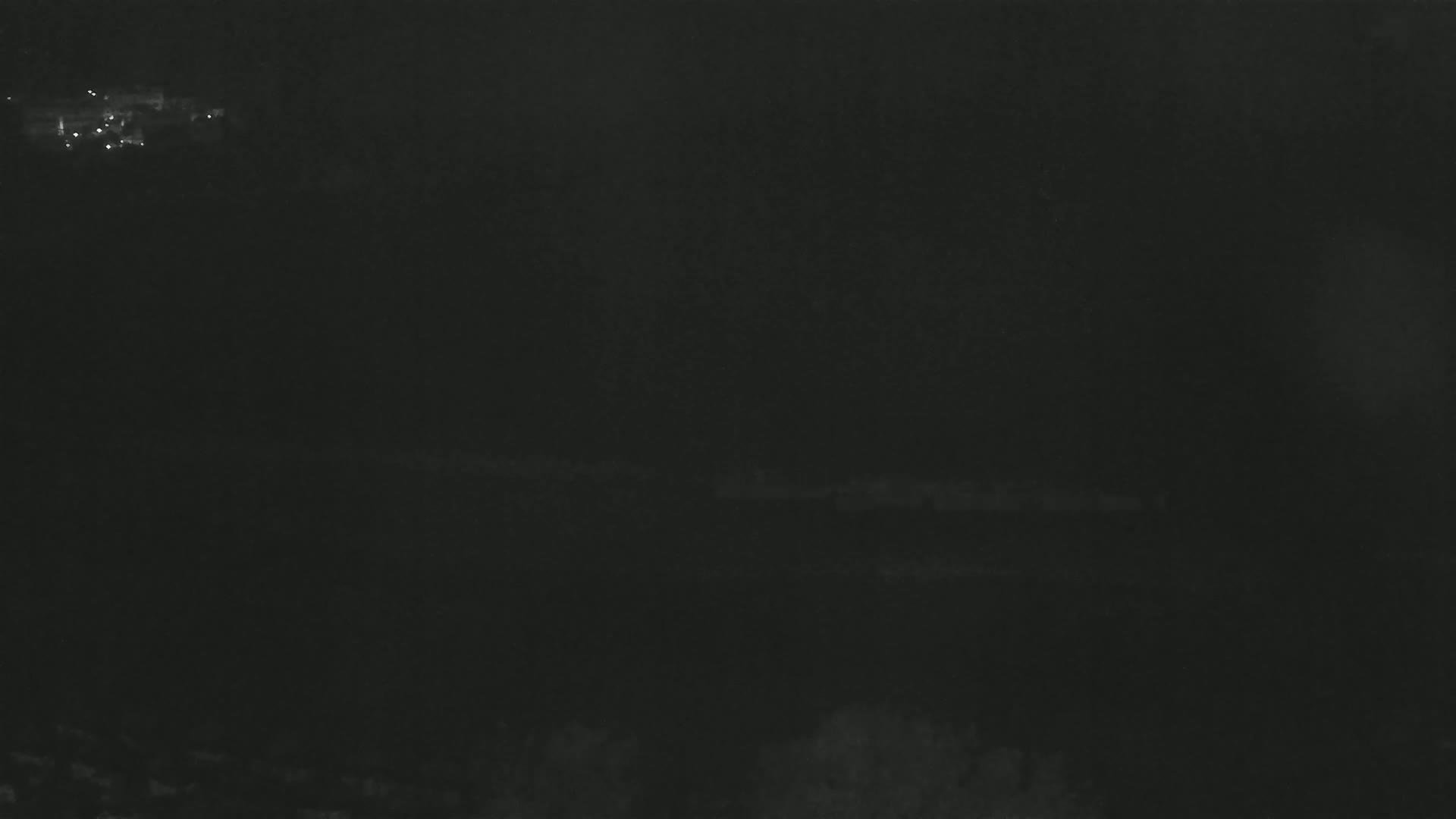 A dark, nighttime scene shows a dimly lit landscape with faint lights in the distance.