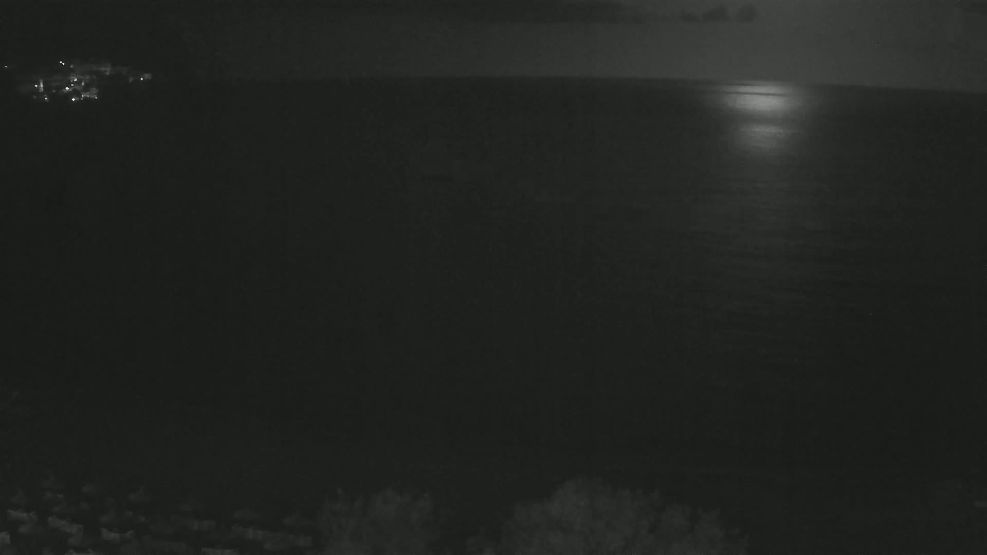 A moonlit nighttime scene shows a dark body of water reflecting the light, with a distant shoreline visible in the upper left corner.
