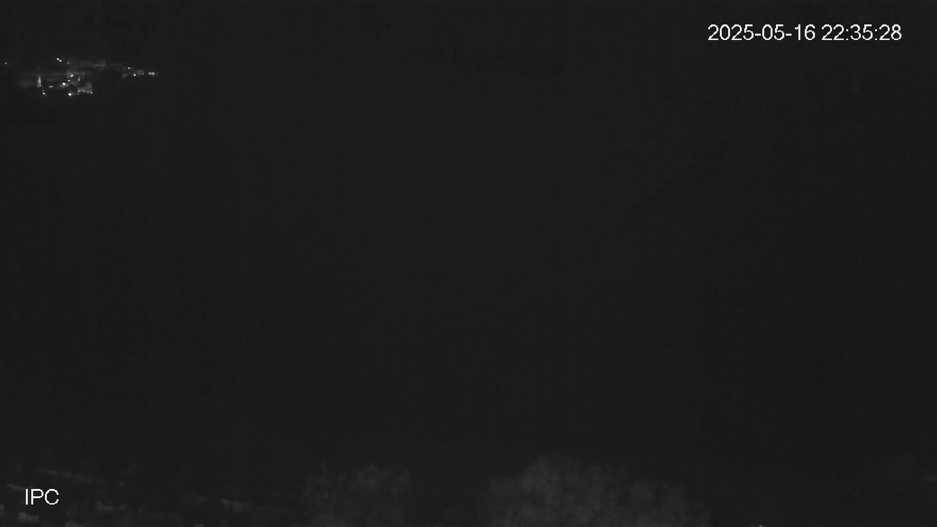 A nighttime, low-light image shows a distant, faintly visible cluster of lights at the top and a dark, indistinct foreground at the bottom.