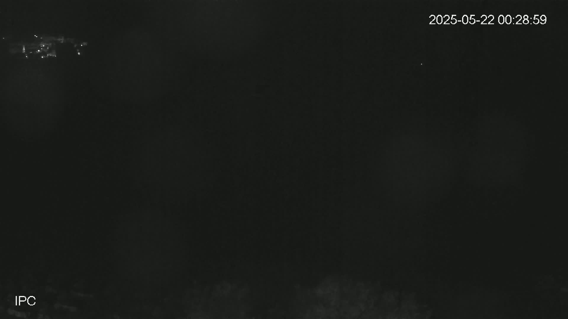 A dark, nighttime scene shows a few distant lights and blurry vegetation at the bottom.